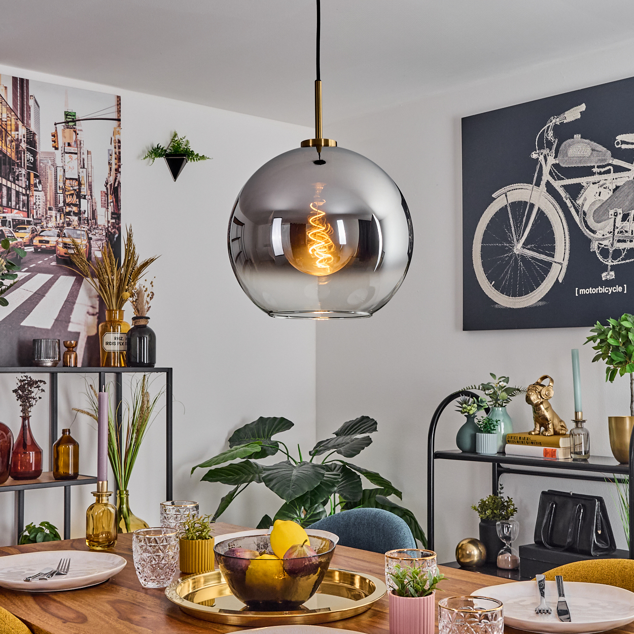 Esszimmer mit großer kugelförmiger Lampe, Tisch mit Obst und Tellern, sowie verschiedenen Dekoelementen.