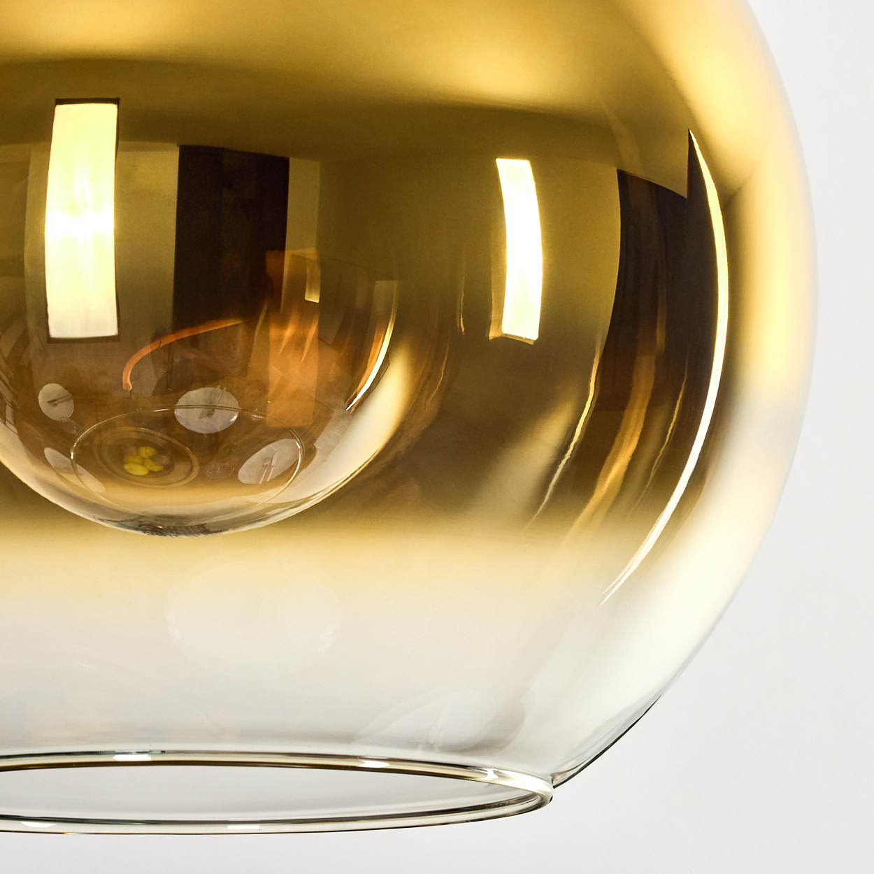 Nahaufnahme einer Glasleuchte mit Goldverlauf. Reflexionen von Lichtern sind sichtbar. Die Basis hat einen silbernen Rand.