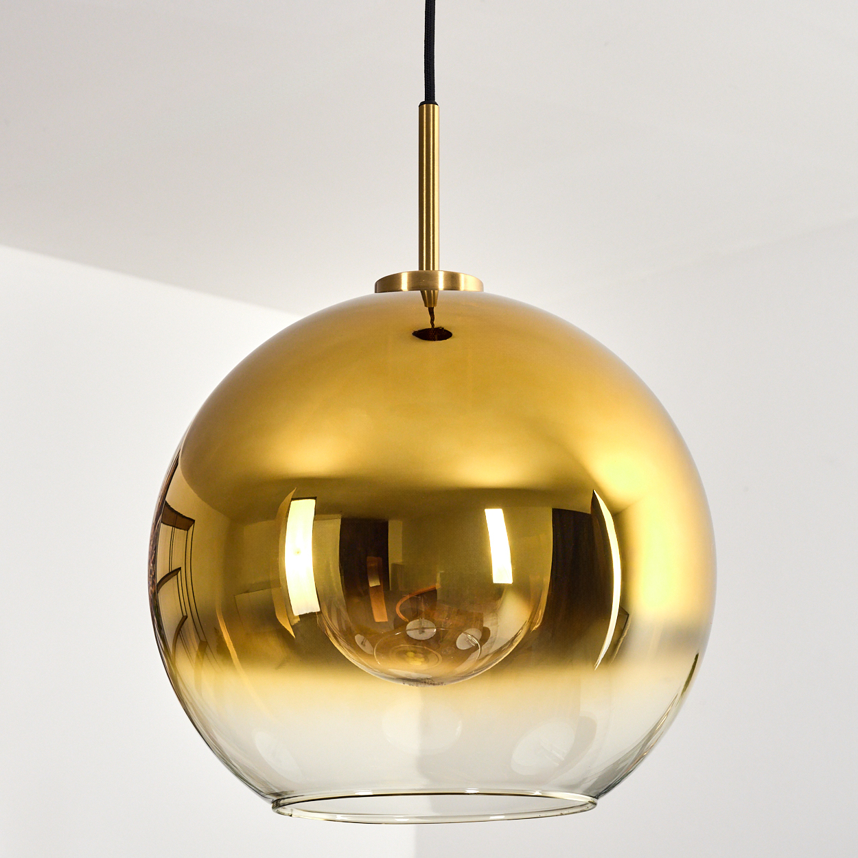 Eine goldene, kugelförmige Pendelleuchte hängt von der Decke. Der untere Teil ist klares Glas, der obere ist goldfarben.