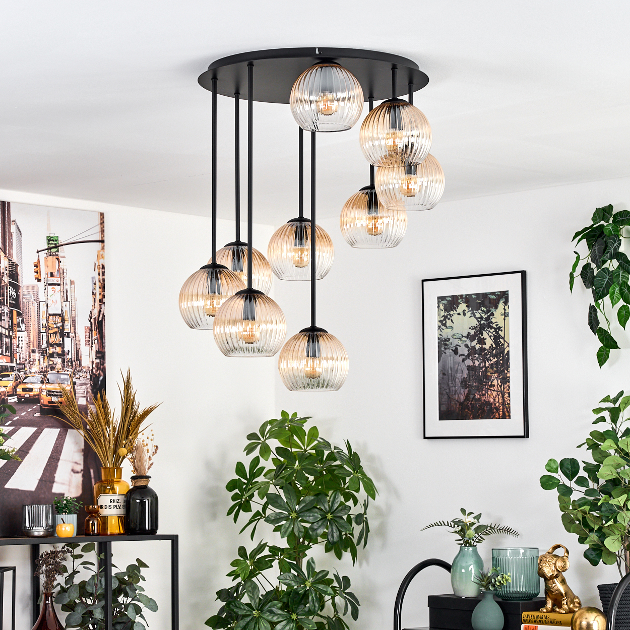 Ein modernes Zimmer mit Kronleuchter, Pflanzen und gerahmter Kunst. Der Kronleuchter hat Glaskugeln. An der Wand befindet sich ein Gemälde einer Stadt.