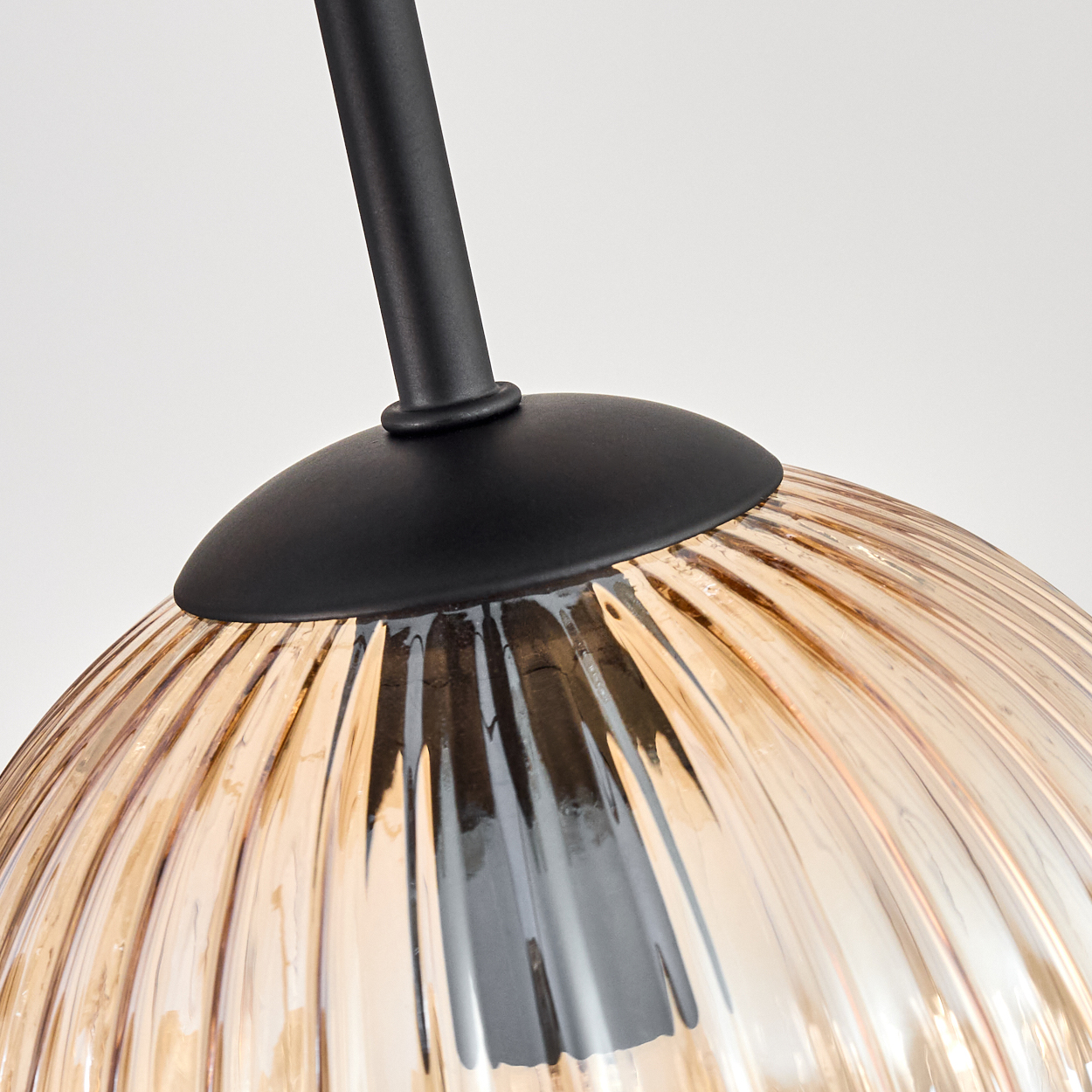 Nahaufnahme einer Lampe. Sie hat einen schwarzen Metallschaft und einen gerippten, bernsteinfarbenen Glasschirm. Weißer Hintergrund.