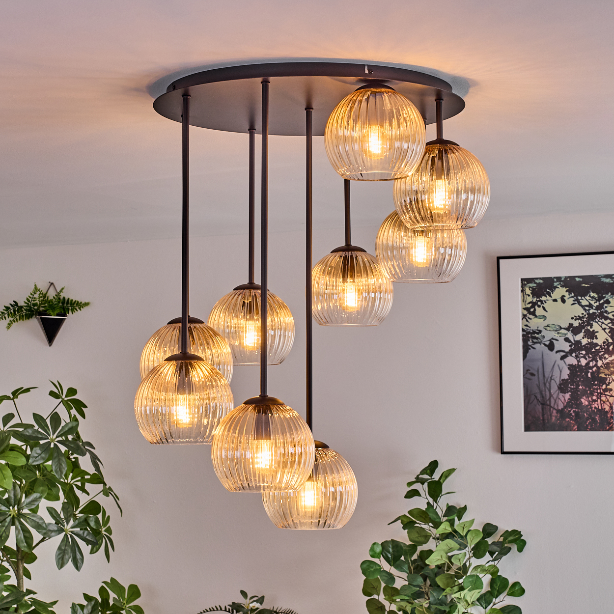 Eine moderne Deckenleuchte mit neun Glaskugelleuchten hängt von der Decke. Pflanzen und gerahmte Kunstwerke sind im Hintergrund.