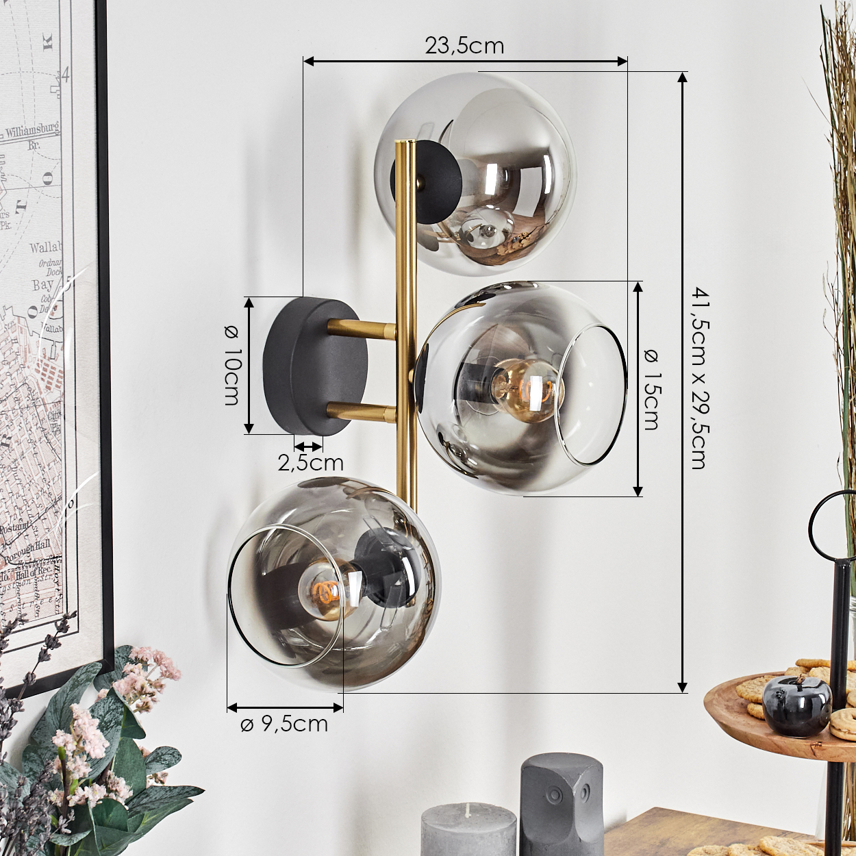 Eine moderne Wandlampe mit drei Glaskugeln. Sie hat einen schwarzen Sockel und goldene Arme. Abmessungen sind angegeben.