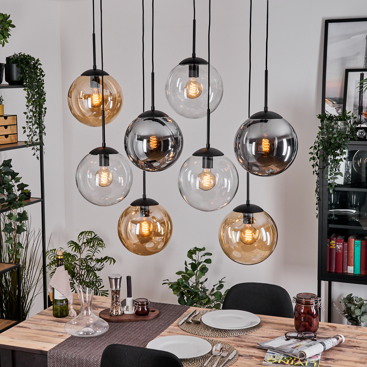 Esszimmer mit Holztisch für das Abendessen. Hängende Kugelleuchten darüber. Pflanzen und Dekoration auf Regalen und Tisch.