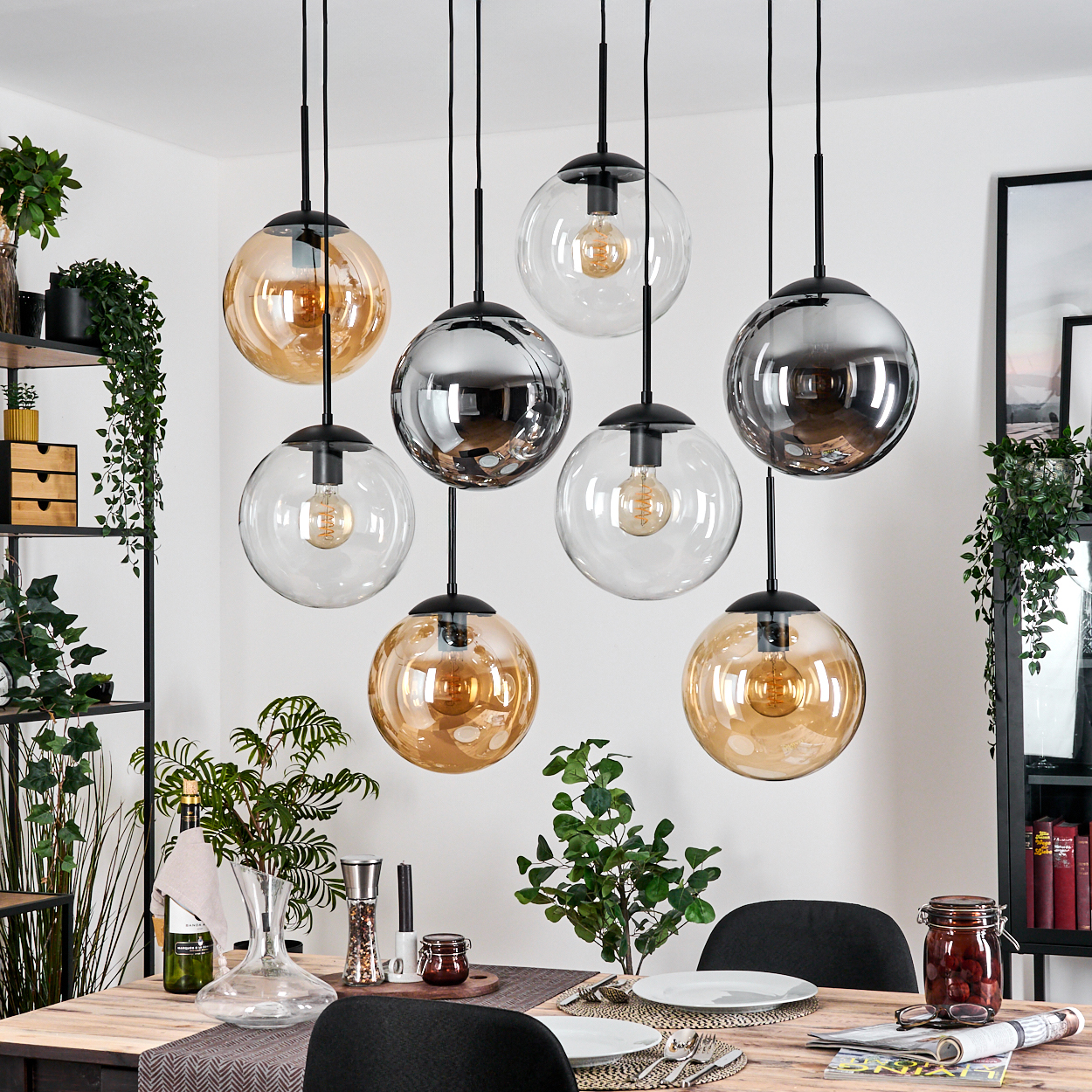 Esszimmer mit hängenden Kugelleuchten. Tisch mit Tellern, Gläsern und Pflanzen. Schwarze Stühle. Regale und gerahmte Kunst im Hintergrund.