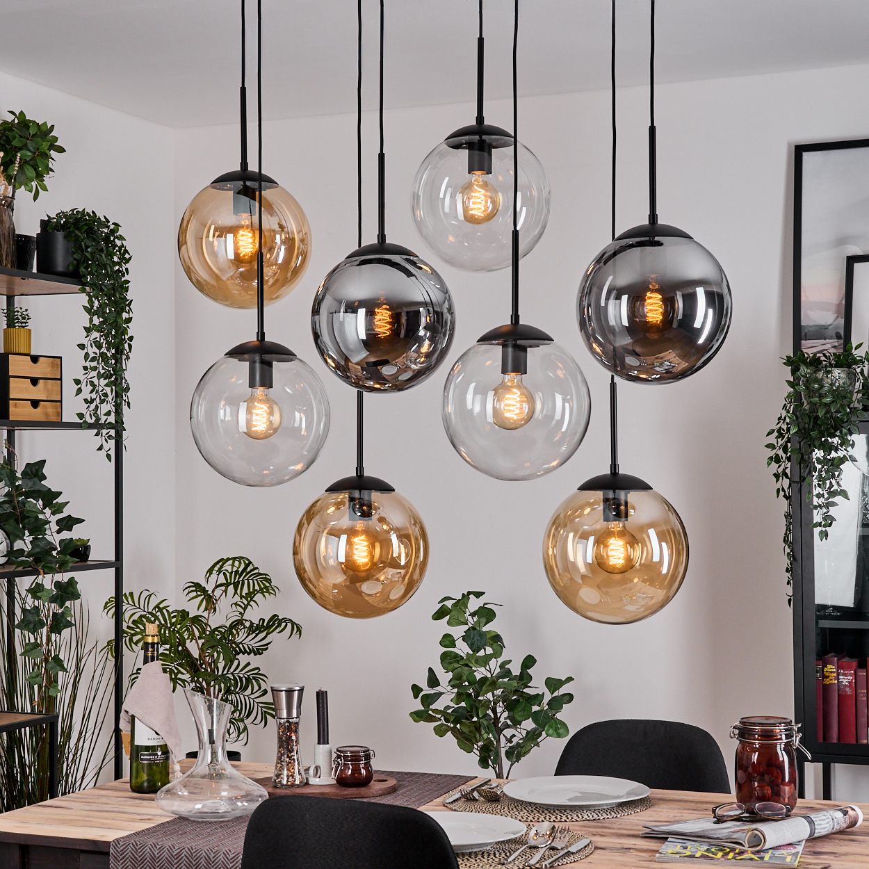 Esszimmer mit Hänge-Kugelleuchten. Tisch mit Pflanzen und Dekoration. Schwarze Stühle und Regale sind sichtbar.