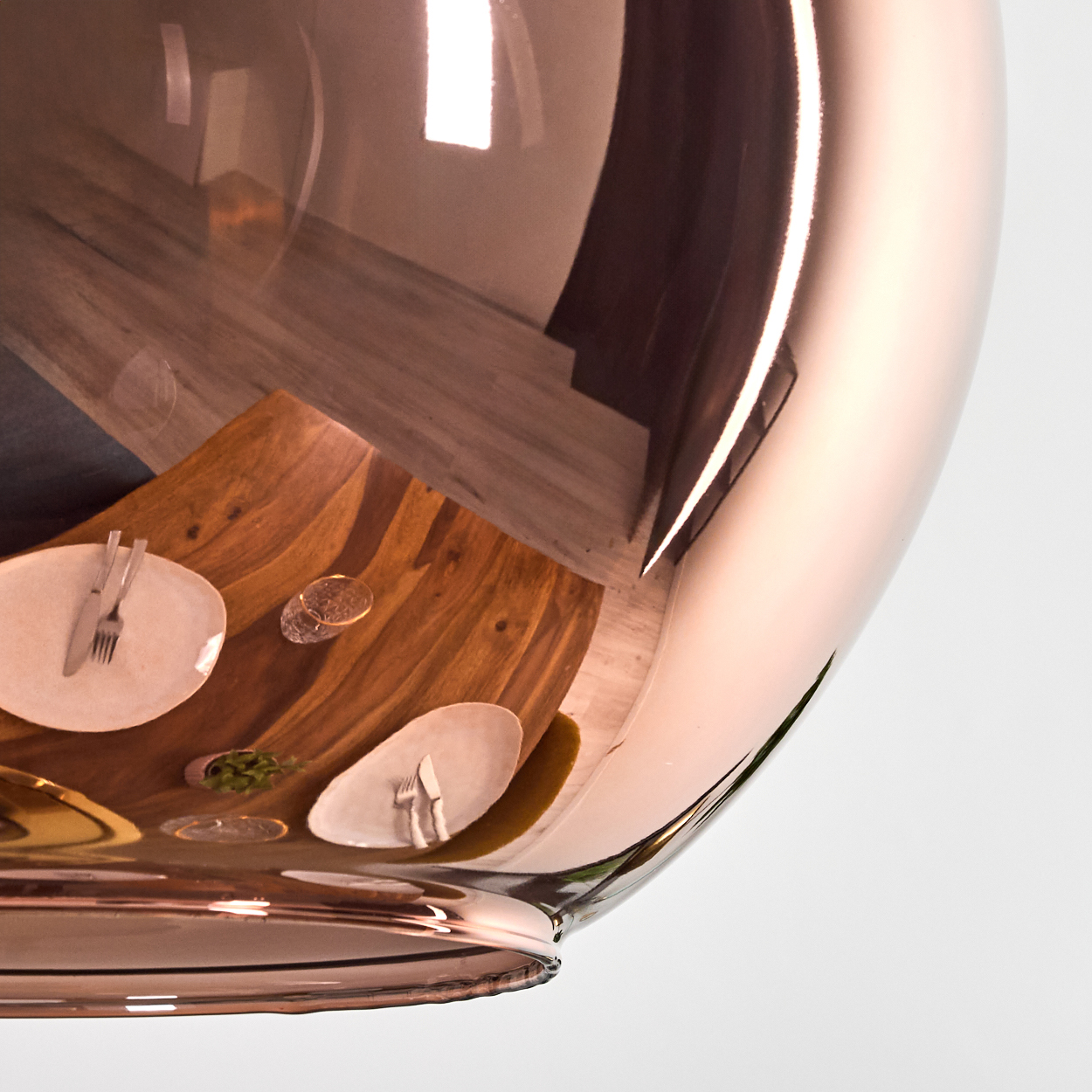 Kupferfarbene Lampe spiegelt einen Tisch mit Tellern, Besteck und einem Glas wider. Holztisch. Weißer Hintergrund.