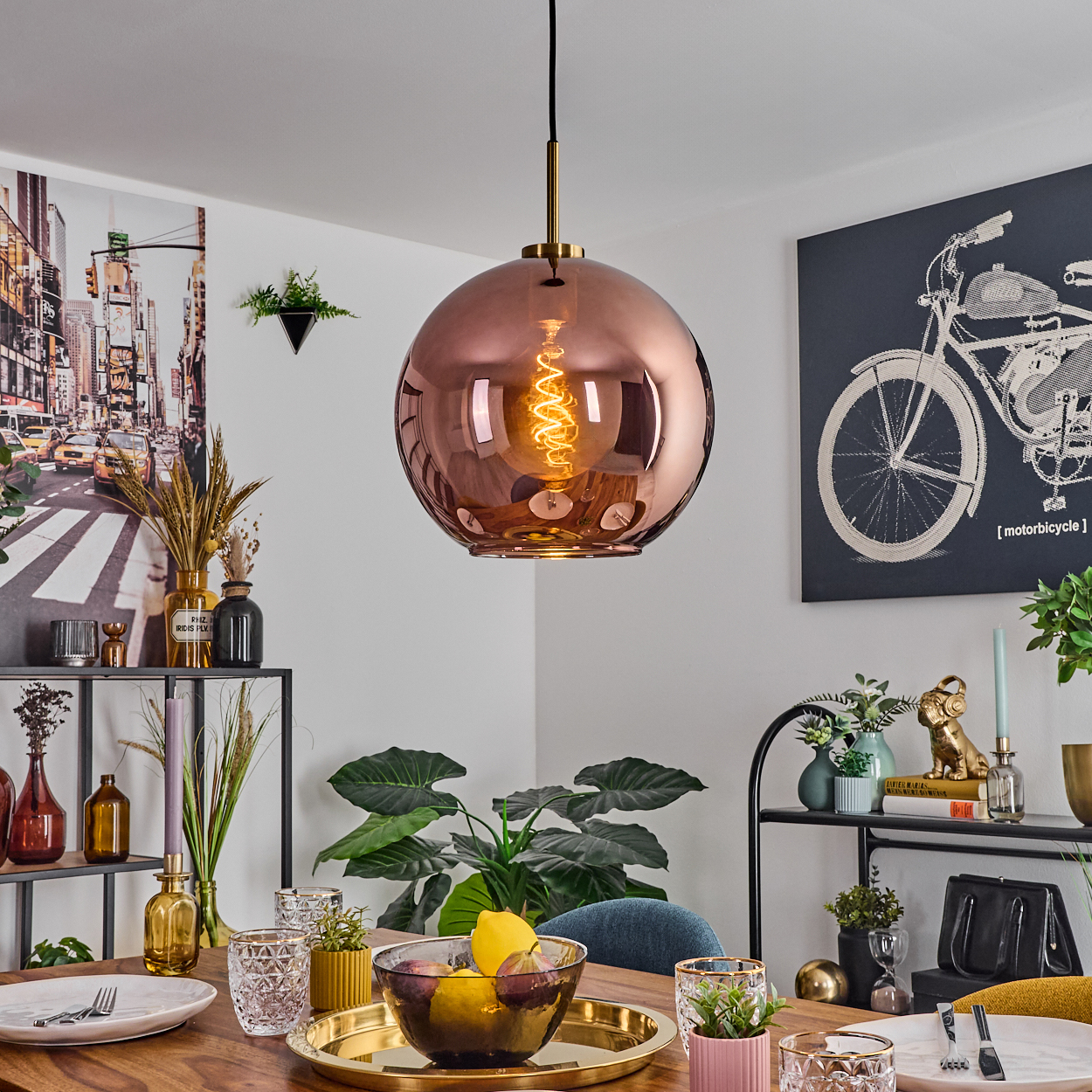 Ein Esszimmer mit einer kupferfarbenen Pendelleuchte, einer Obstschale und einem Fahrradkunstwerk.