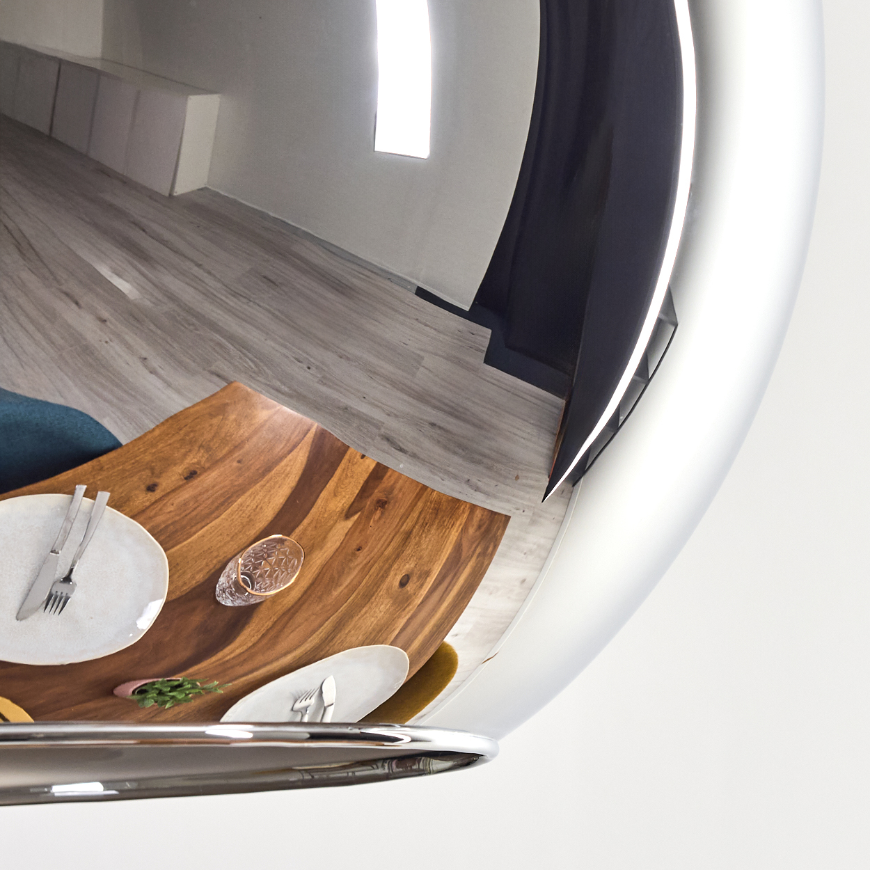Eine reflektierende Oberfläche zeigt einen Holztisch mit Tellern und Besteck. Der Hintergrund zeigt einen Raum mit Holzboden und einem Fenster.