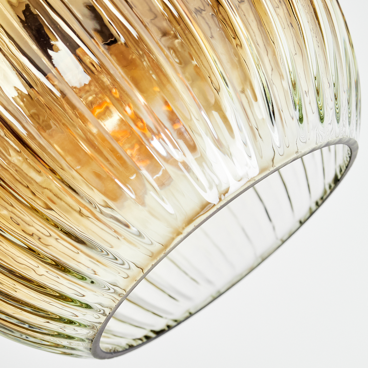 Nahaufnahme eines Lampenschirms aus Glas mit vertikalen Rippen. Das Glas ist bernsteinfarben, im Inneren ist eine Lichtquelle sichtbar. Weißer Hintergrund.