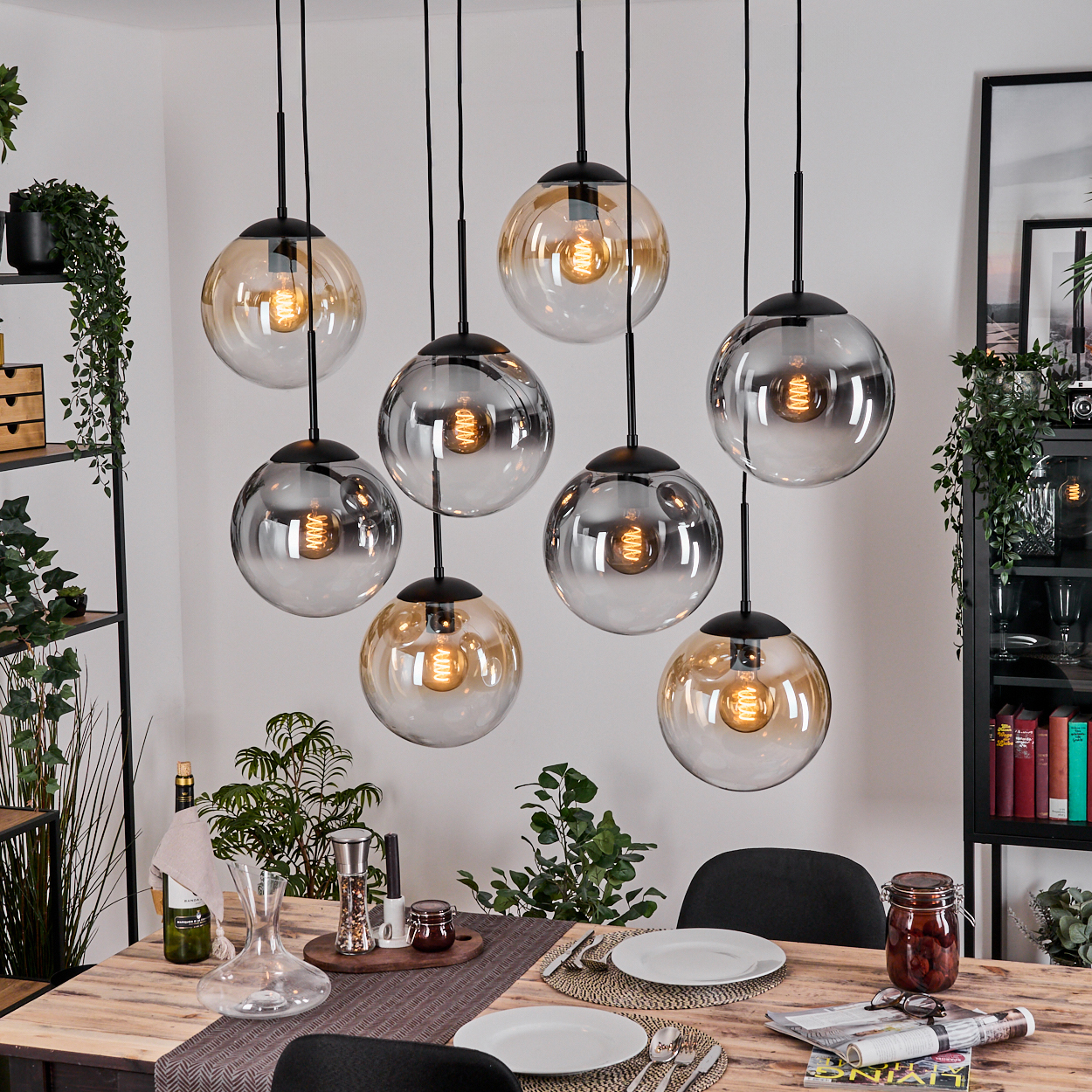Esszimmer mit Holztisch, Hängeleuchten und Tischdeko. Pflanzen und dekorative Gegenstände im Hintergrund.