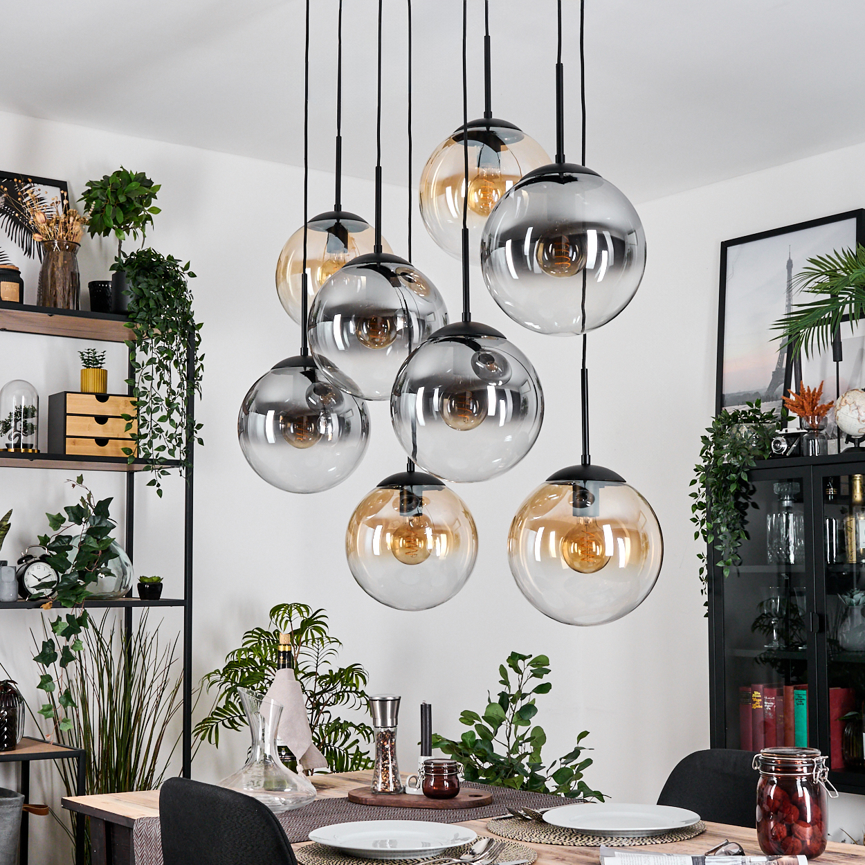 Esszimmer mit hängenden Kugelleuchten. Tisch mit Tellern und Dekoration. Regale mit Pflanzen und ein Schrank mit Dekorartikeln.