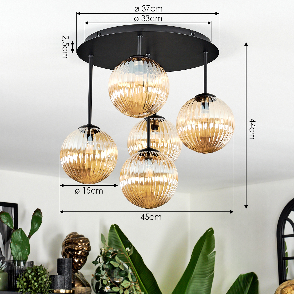 Eine moderne Deckenlampe mit fünf kugelförmigen, gerippten, bernsteinfarbenen Glasschirmen. Die Lampe ist schwarz, mit Maßangaben.