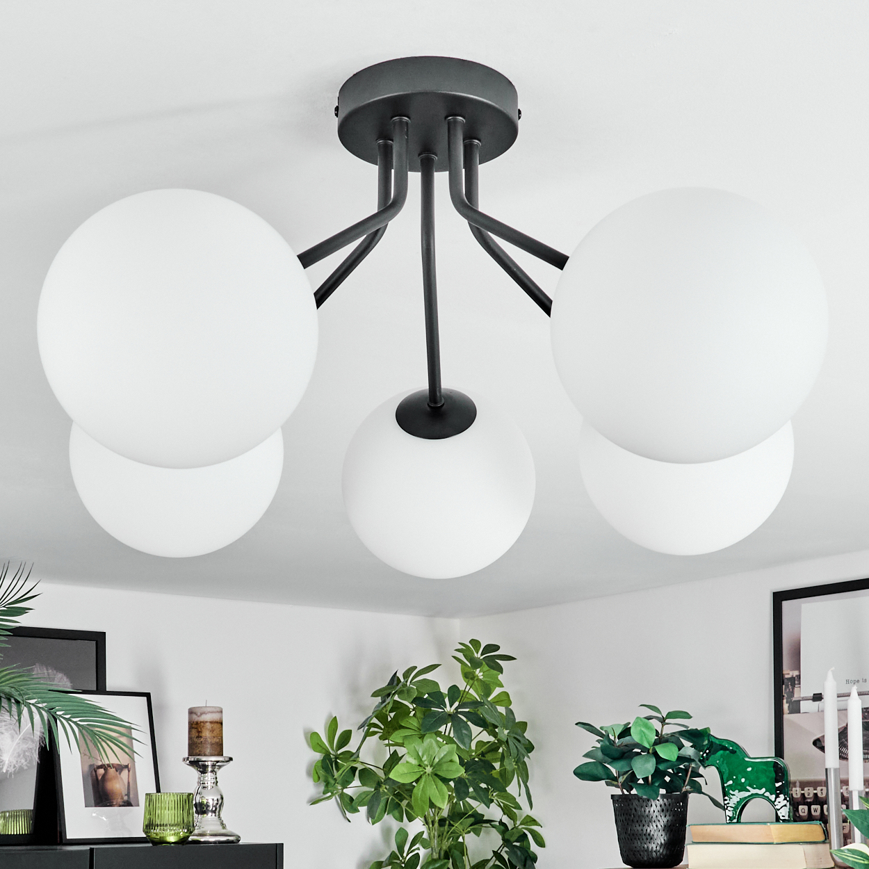 Eine moderne Deckenlampe mit fünf weißen Kugeln. Schwarze Metallarme und Deckenhalterung. Pflanzen und Dekoration darunter, weiße Decke.