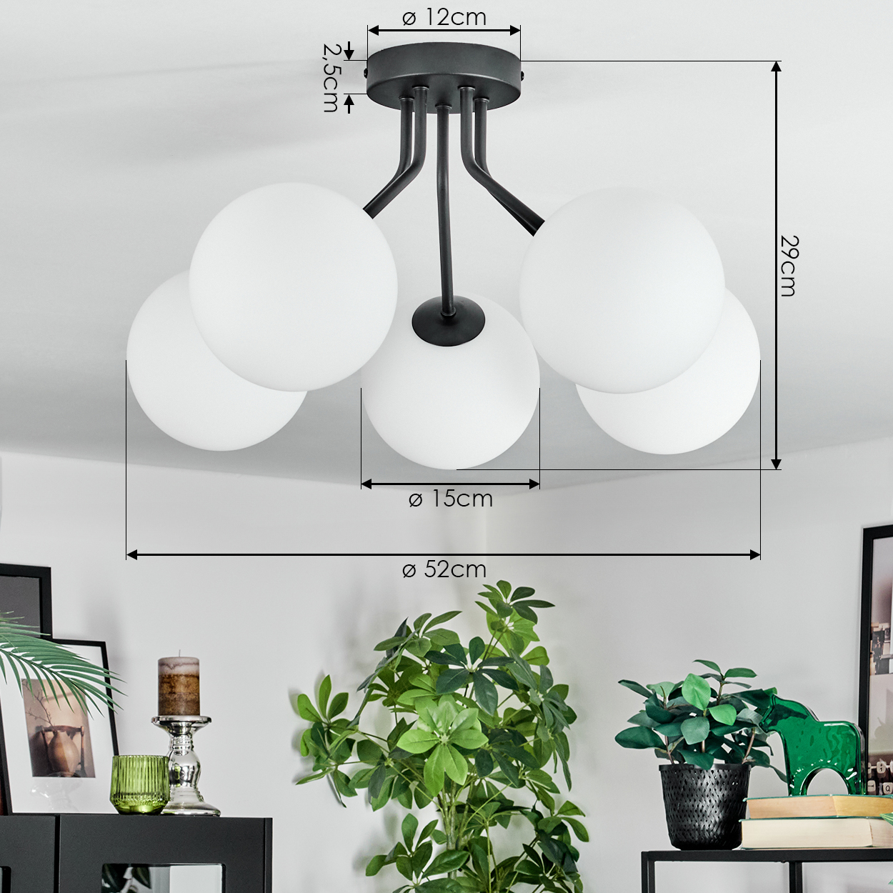 Moderne Deckenlampe mit fünf weißen Glaskugeln. Schwarzer Metallrahmen. Maße werden angezeigt. Pflanzen und Deko im Vordergrund.