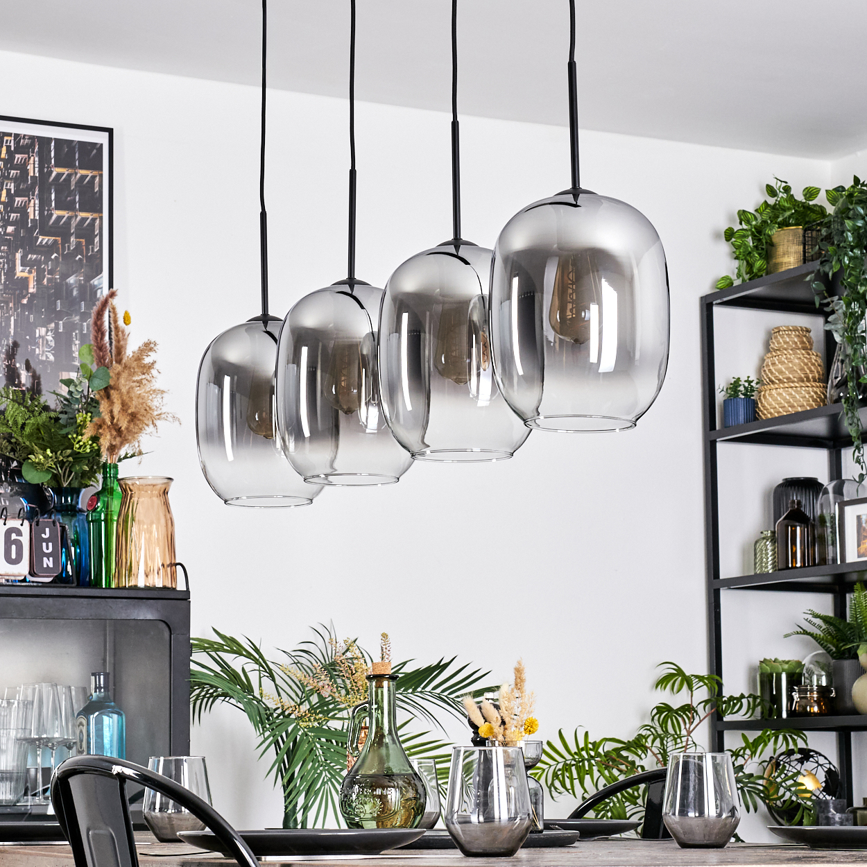 Esszimmer mit hängenden Glaslampen. Tisch mit Gläsern und Pflanzen. Regale mit Dekorationen. Pflanzen und Wandkunst.