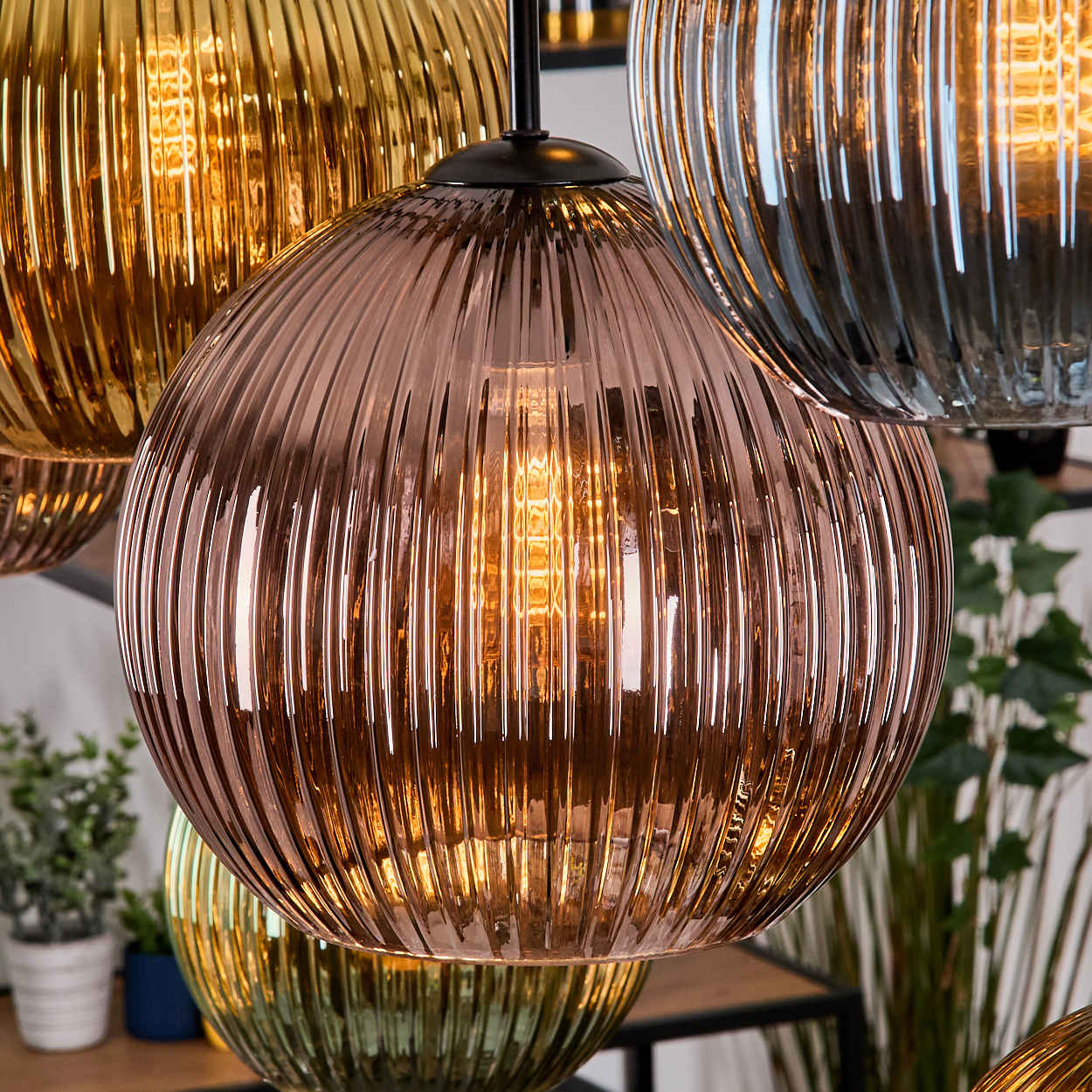 Nahaufnahme von hängenden Glaslampen mit Rippendesign. Die Lampen sind in verschiedenen Farben gehalten und haben warme, leuchtende Glühbirnen.