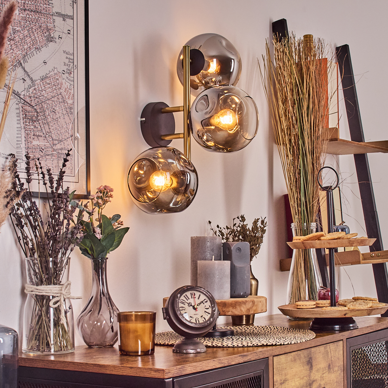 Dekorative Szene mit Wandlampe, Blumen, Kerzen und Uhr auf einem Holztisch. Karte und Leiter sind ebenfalls sichtbar.