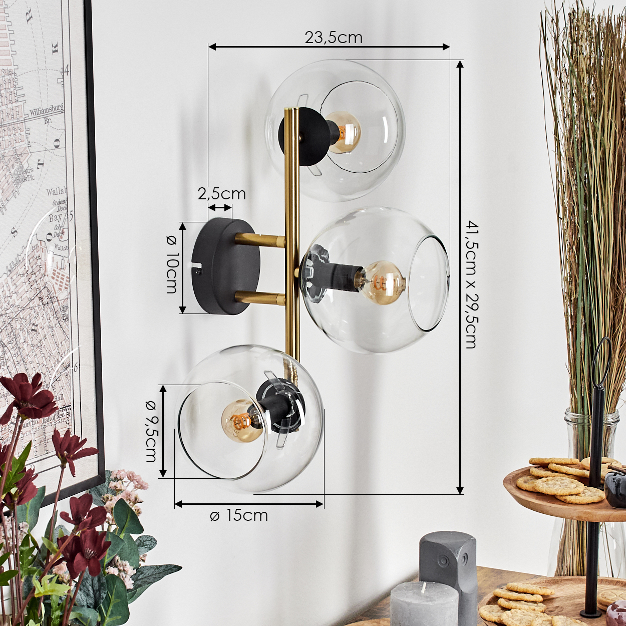 Moderne Wandlampe mit drei Glaskugeln, schwarzen und goldenen Akzenten. Maße werden angezeigt. Blumen und Essen sind ebenfalls vorhanden.
