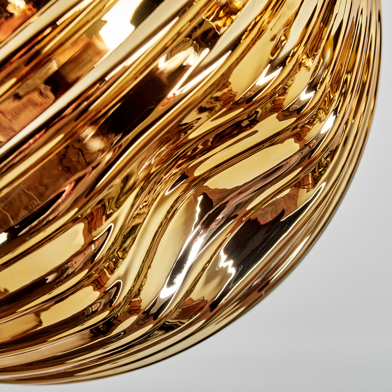 Nahaufnahme eines goldenen, reflektierenden Objekts mit wellenartigen Mustern. Die Oberfläche ist glänzend und reflektiert Licht.