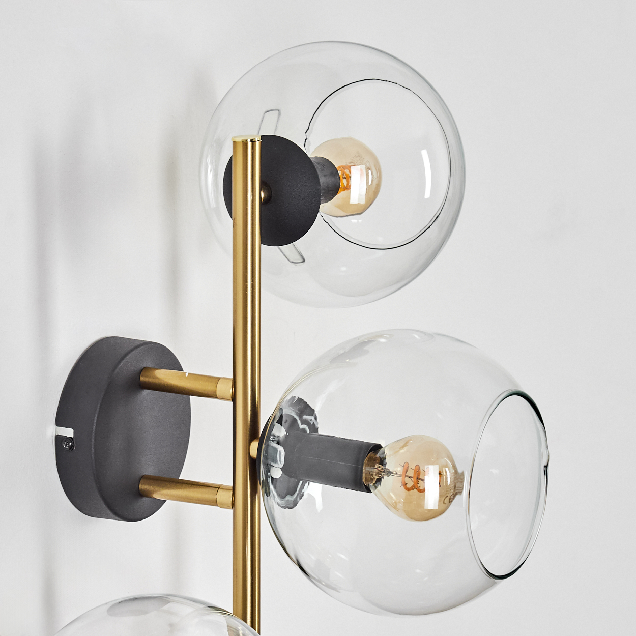 Eine moderne Wandleuchte mit drei Glasschirmen. Die Leuchte hat eine gold-schwarze Oberfläche und ist an einer weißen Wand montiert.