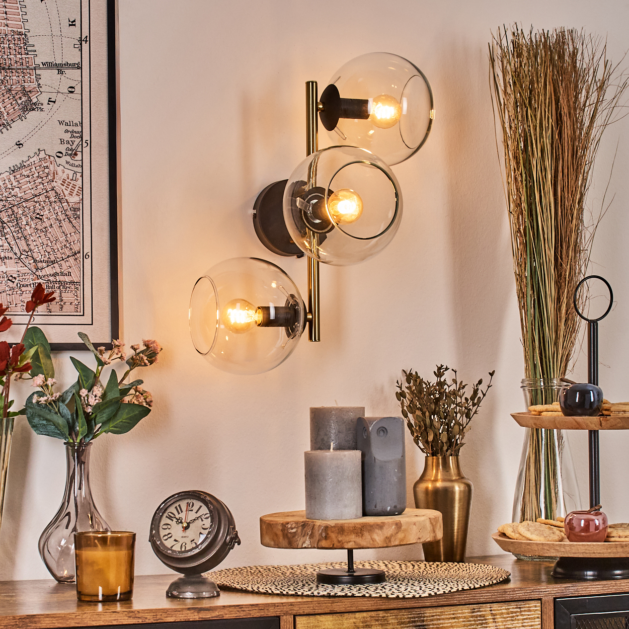 Ein Raum mit Wandlampe, Kerzen, Uhr, Blumen und Dekorationen auf einem Holztisch. Eine Karte hängt an der Wand.