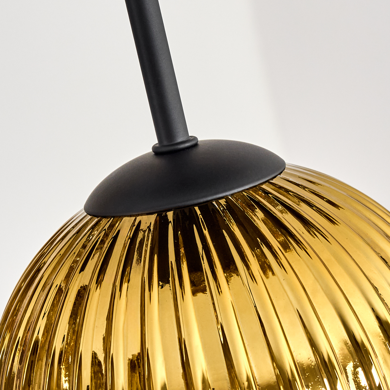 Nahaufnahme eines goldenen Glaslampenschirms mit vertikalen Rippen, schwarzem Metallschaft und Sockel vor weißem Hintergrund.