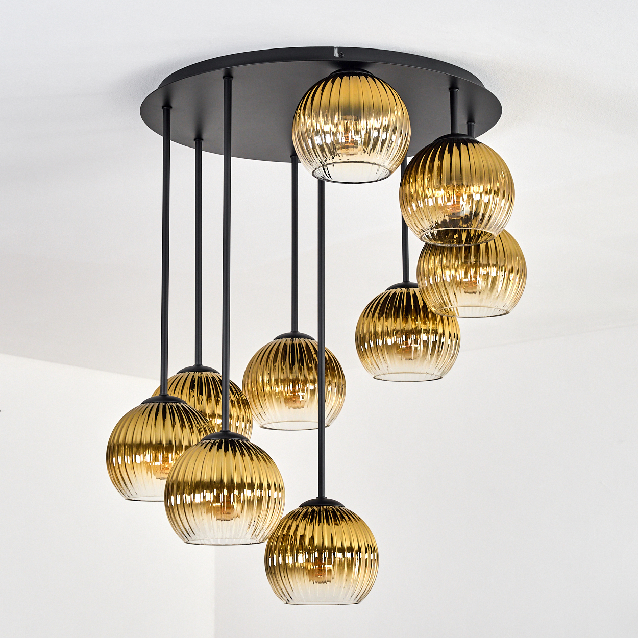 Eine moderne Deckenleuchte mit mehreren goldfarbenen Glaskugeln hängt von einer schwarzen kreisförmigen Basis ab.