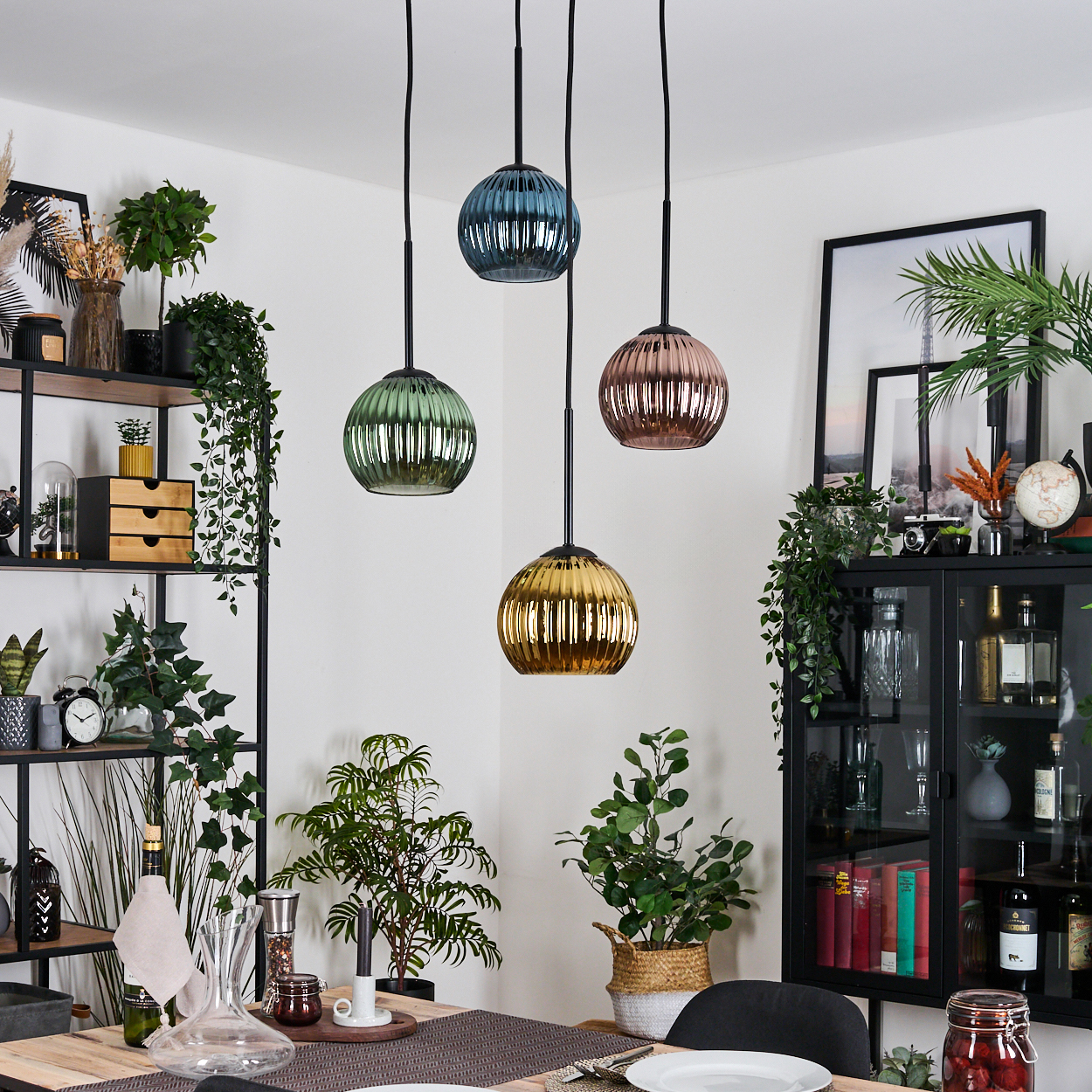 Esszimmer mit Hängelampen. Verschiedene Pflanzen und Möbel sind sichtbar. Die Lampen haben verschiedene Farben, darunter Blau, Grün und Gold.