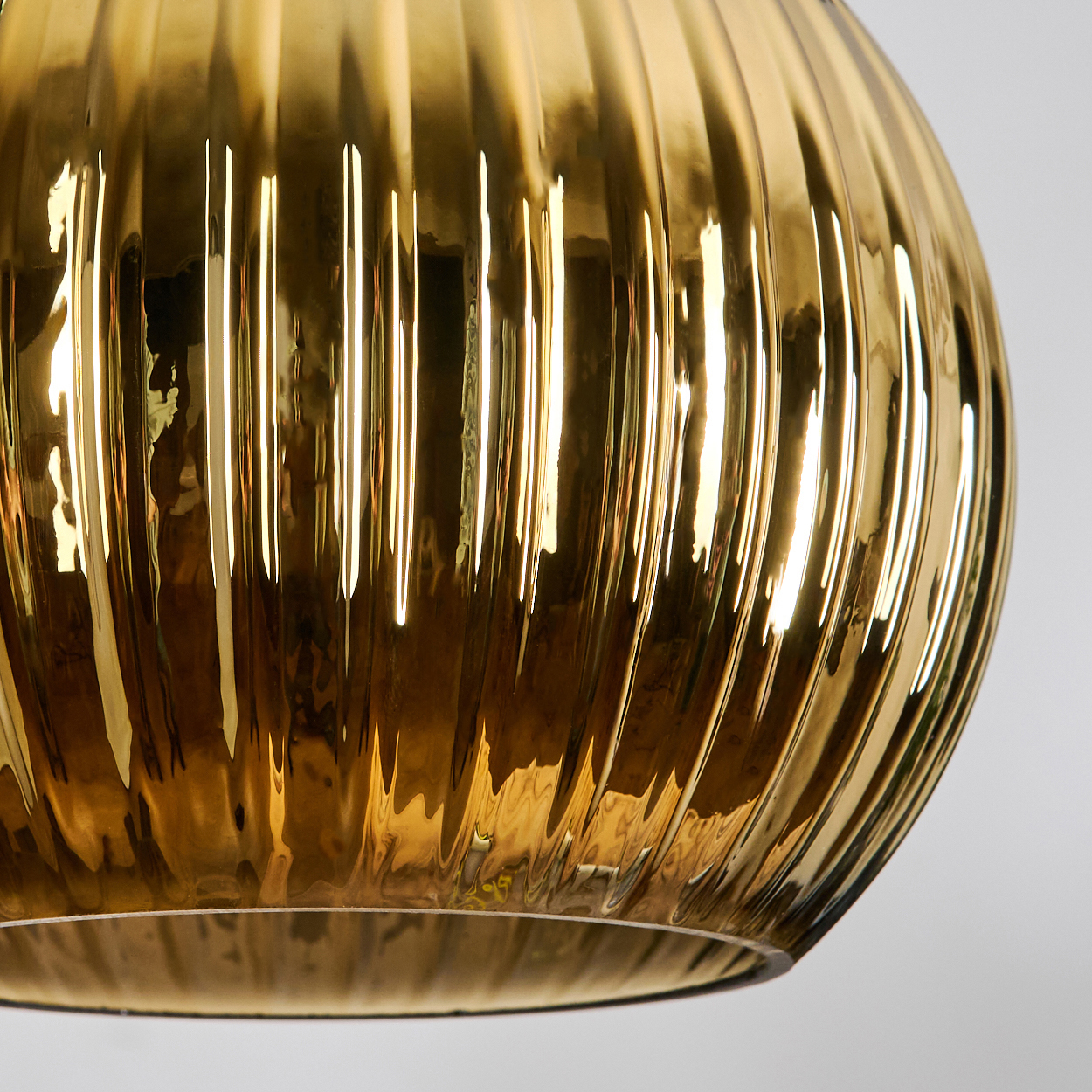 Nahaufnahme eines goldenen Glasobjekts mit vertikalen Rippen. Das Objekt reflektiert Licht und erzeugt Glanzlichter. Der Hintergrund ist weiß.