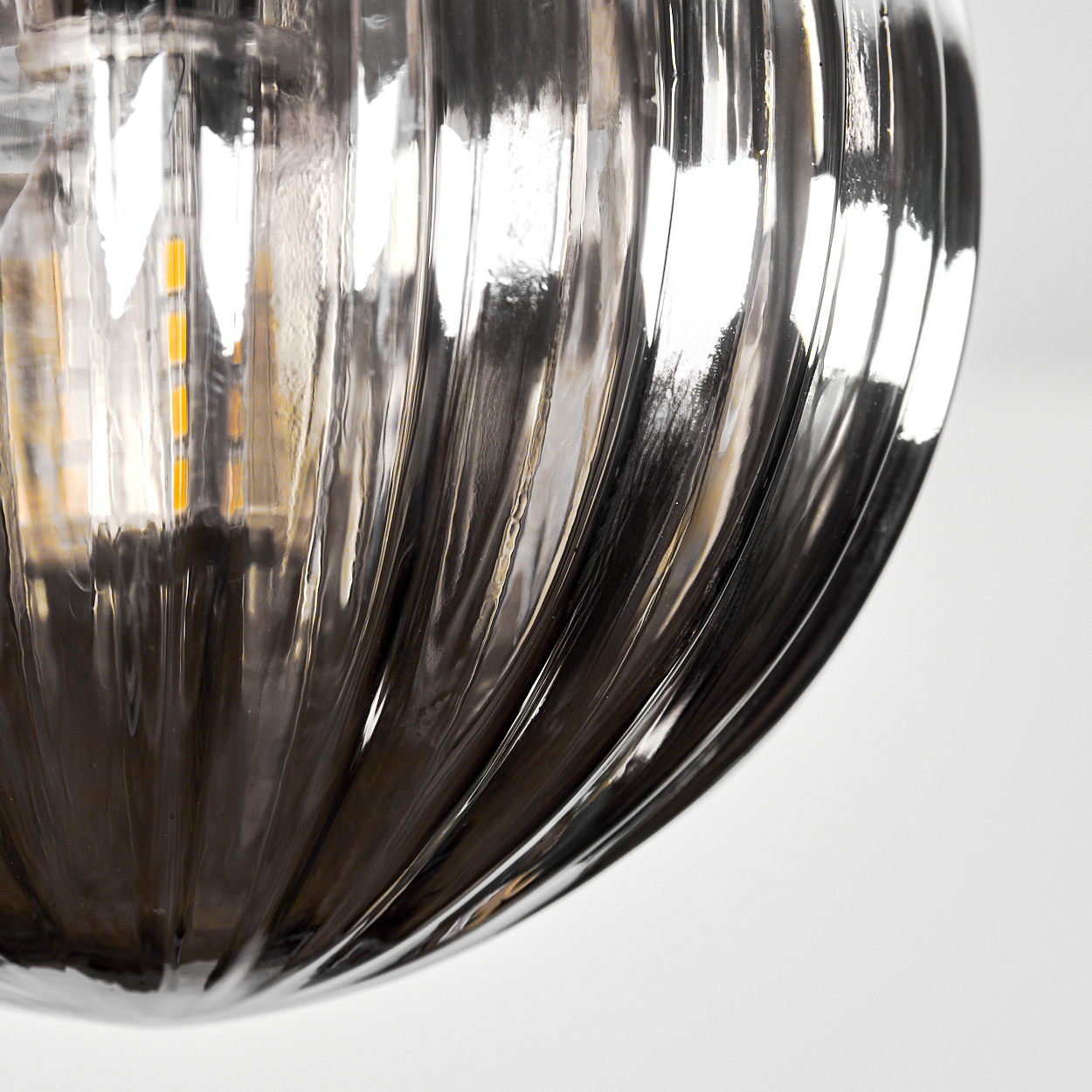 Nahaufnahme einer gerippten Glasglühbirne. Das Glas ist reflektierend mit dunklem, metallischem Aussehen. Im Inneren ist gelbes Licht sichtbar.