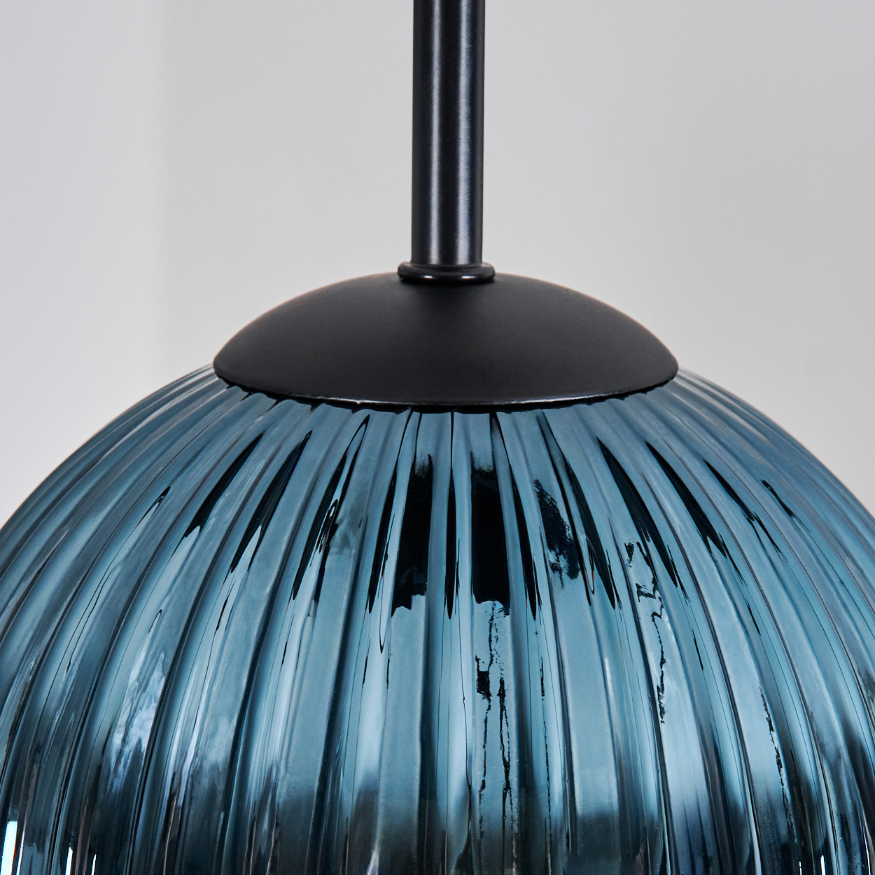 Nahaufnahme eines blauen Glaslampenschirms mit vertikalen Rippen, schwarzen Metallbeschlägen und weißem Hintergrund.