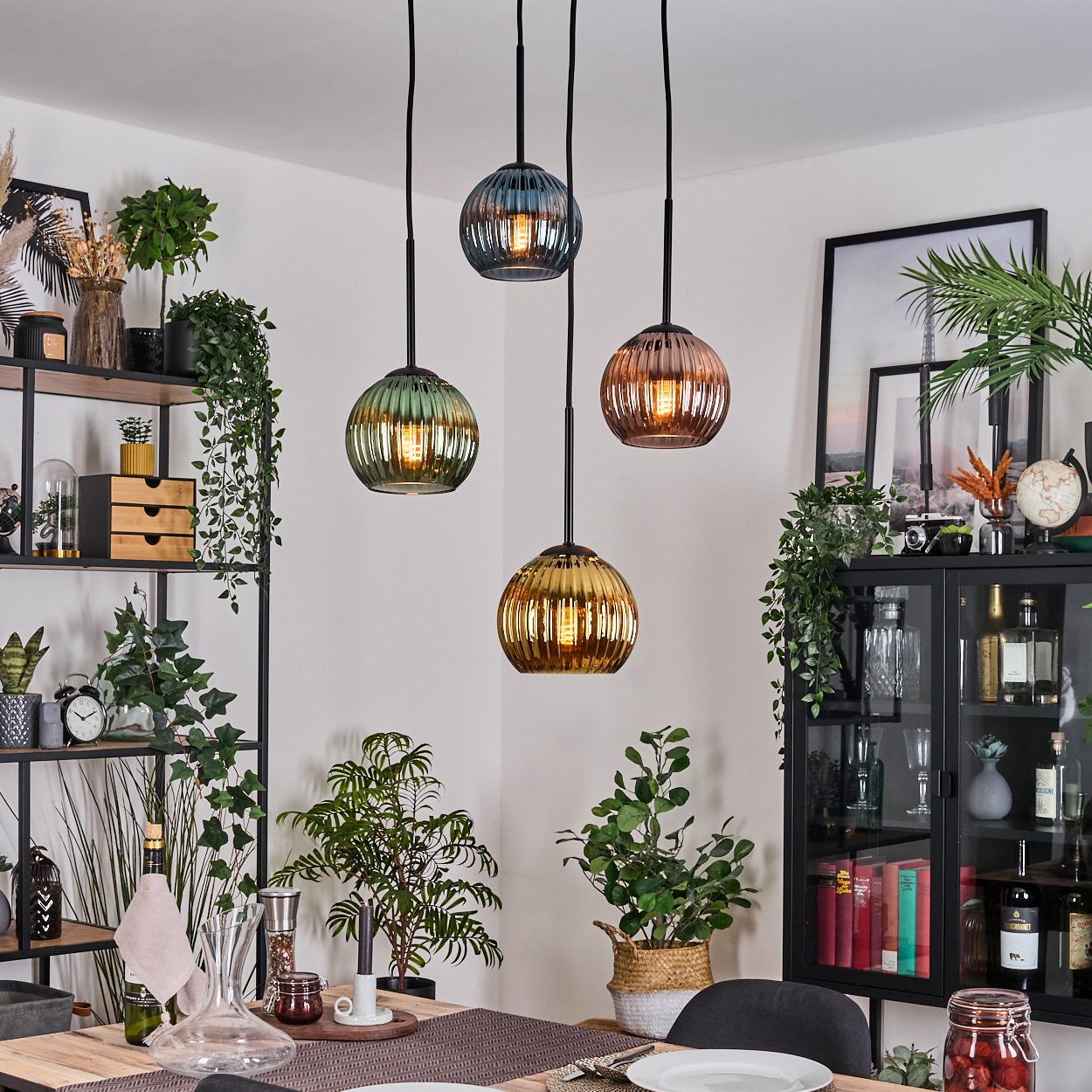 Esszimmer mit vier bunten Pendelleuchten. Pflanzen und Dekorationen umgeben einen Tisch für eine Mahlzeit. Schwarzer Schrank ist sichtbar.