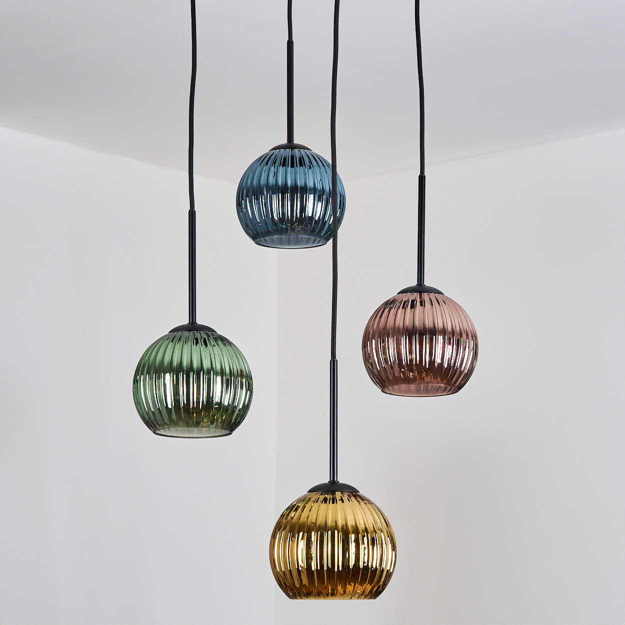 Vier bunte Pendelleuchten hängen von der Decke. Jede hat eine andere Farbe: grün, blau, rosa und gold. Weiße Wände.