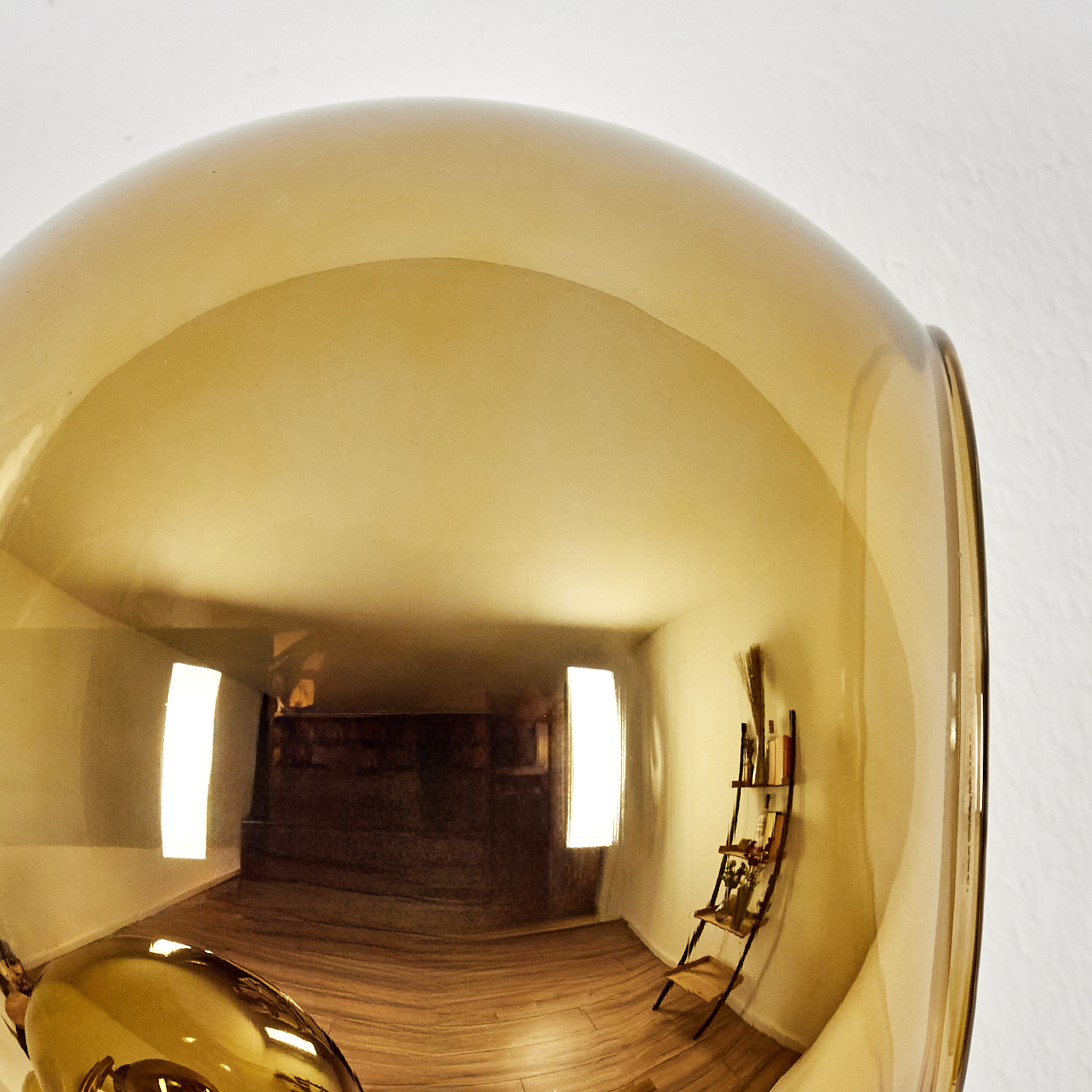Ein klares, bernsteinfarbenes Glasobjekt reflektiert einen Raum mit Holzböden, zwei Fenstern und einem kleinen Bücherregal.