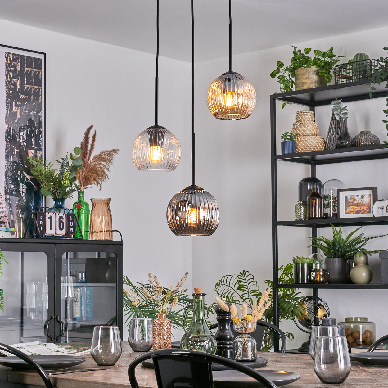 Esszimmer mit Hängelampen, Tisch, Regalen mit Pflanzen und Dekoration. Deckenleuchten sind an.