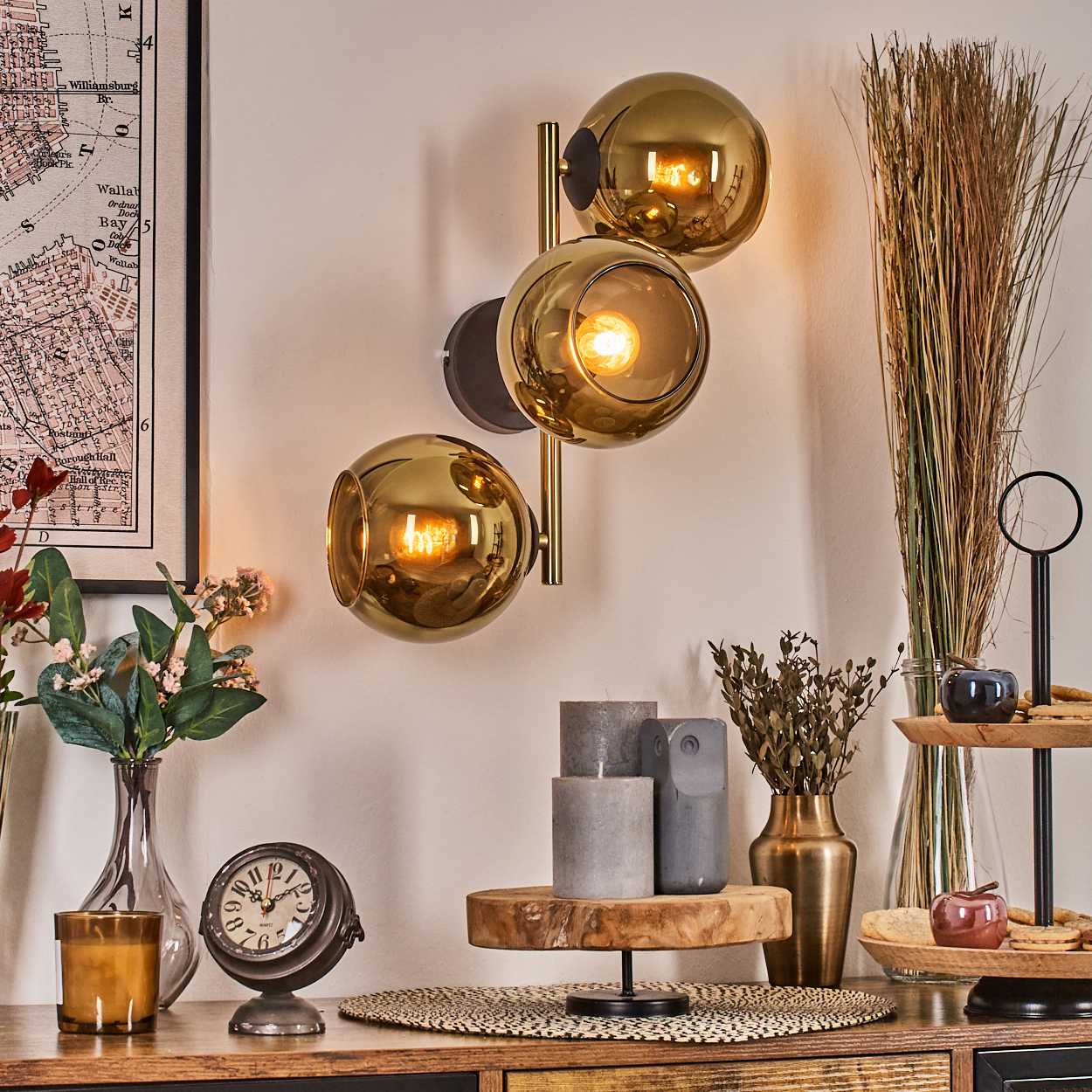 Ein Raum mit Wandlampe, Uhr, Blumen, Kerzen und Karte. Warme Beleuchtung und dekorative Elemente schaffen eine gemütliche Atmosphäre.