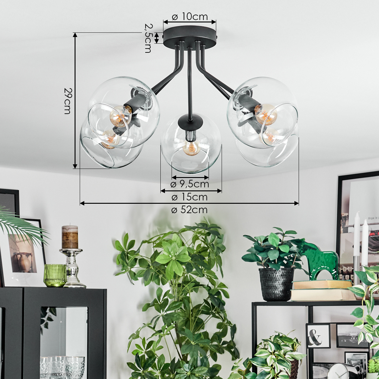 Eine moderne Deckenlampe mit fünf Glaskugeln. Abmessungen sind angegeben. Im Hintergrund sind grüne Pflanzen und Möbel zu sehen.