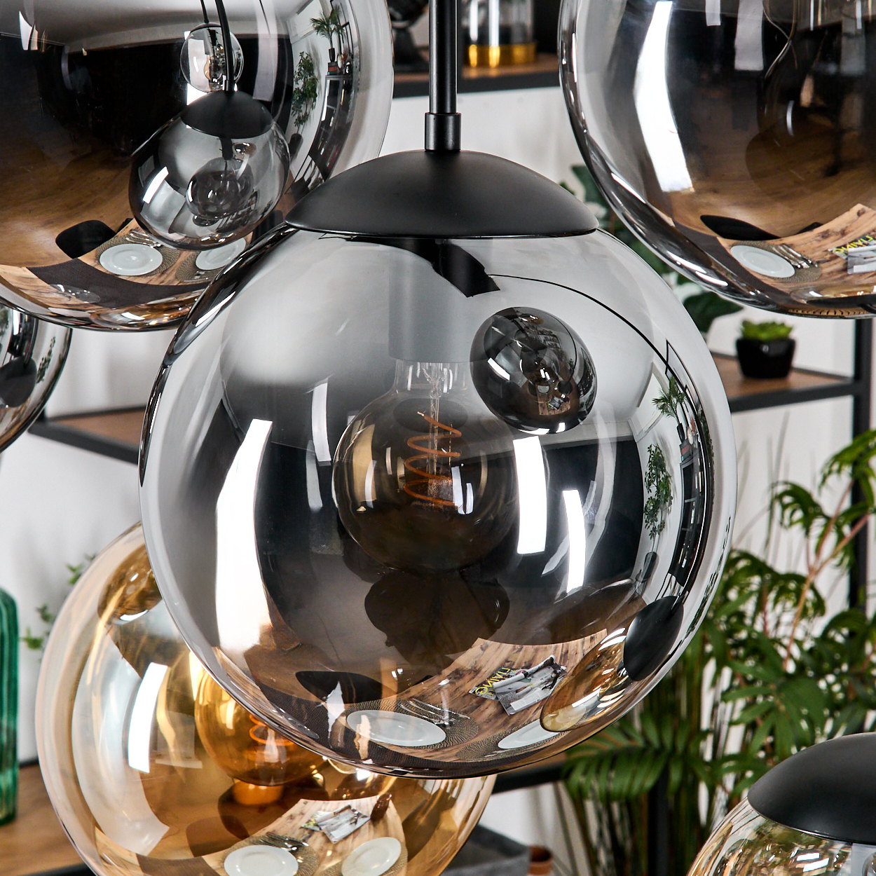 Nahaufnahme einer modernen Deckenlampe mit mehreren kugelförmigen Glasschirmen. Die Schirme reflektieren den Raum und enthalten Edison-Glühbirnen.