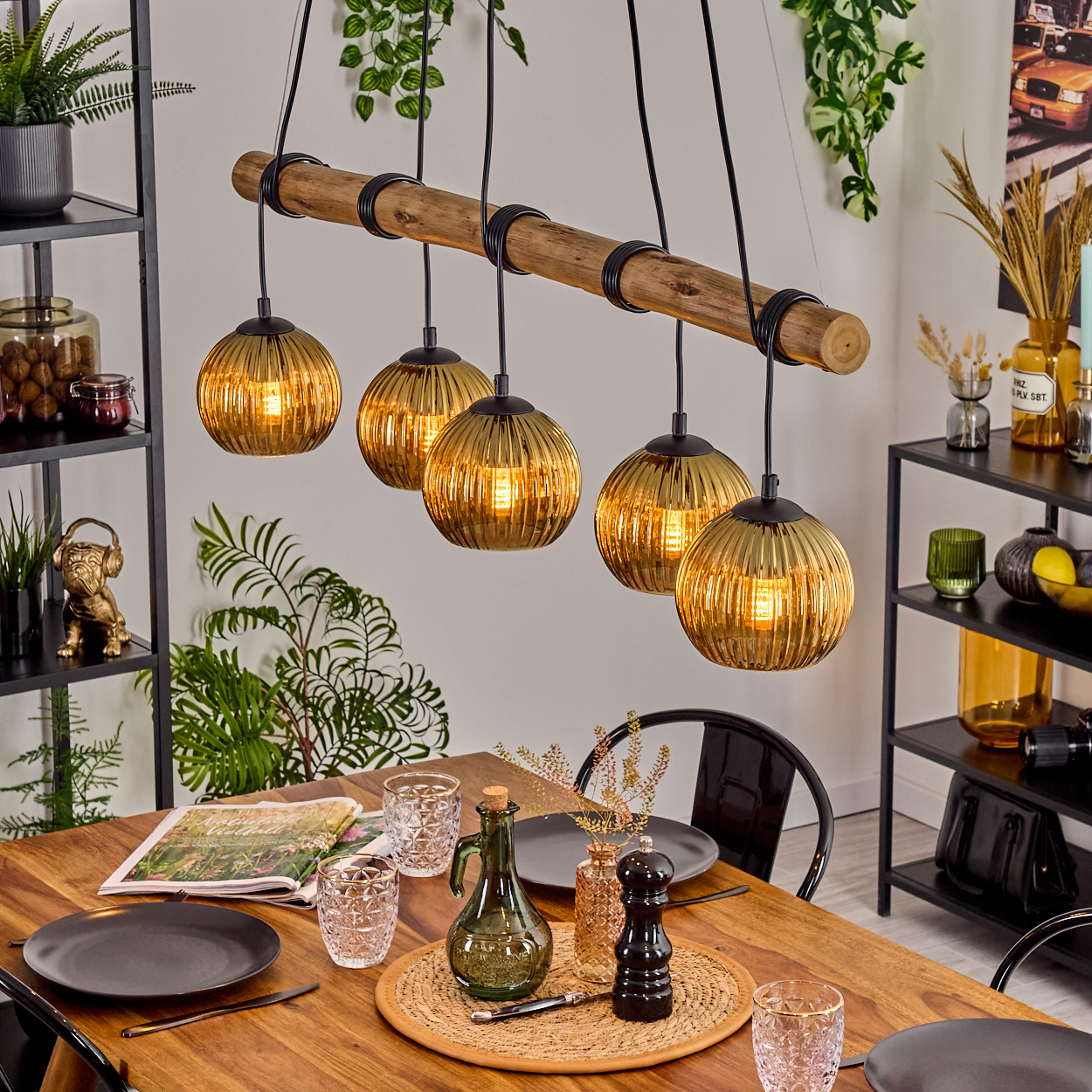 Esszimmer mit Holztisch, Glas-Pendelleuchten und Dekoration. Teller, Gläser und Pflanzen auf dem Tisch und in Regalen.