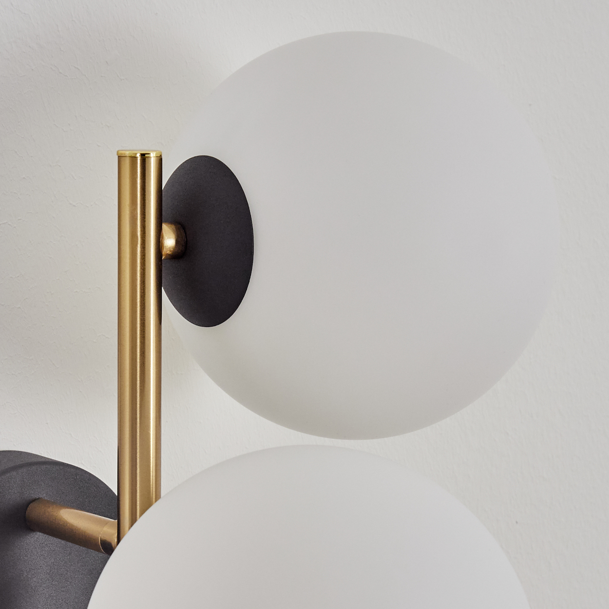Nahaufnahme einer modernen Wandleuchte. Sie hat drei weiße Kugelschirme, Messingarme und schwarze Halterungen an einer weißen Wand.