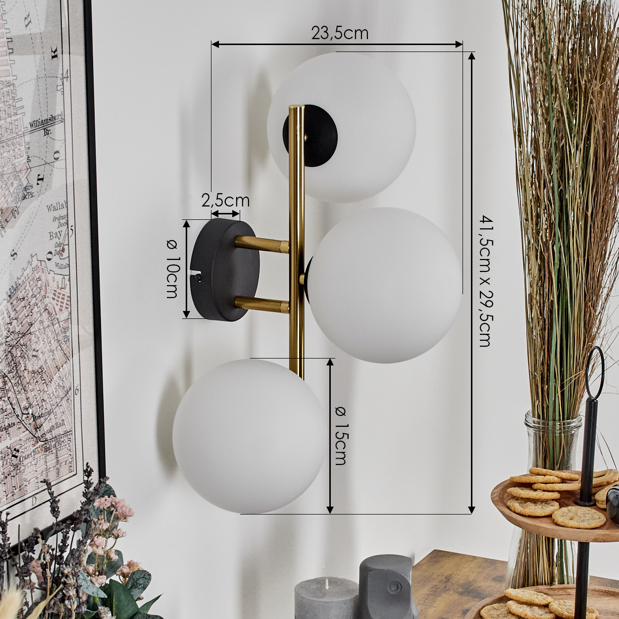 Eine Wandlampe mit drei weißen Kugelleuchten. Maße sind auf dem Bild angegeben. Eine Karte, eine Vase mit Zweigen und Kekse sind ebenfalls sichtbar.