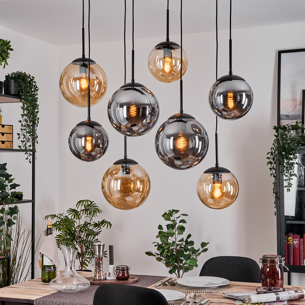 Esszimmer mit Holztisch, Hängeleuchten, Pflanzen und schwarzem Stuhl. Die Lampen haben bernsteinfarbenes und graues Glas.