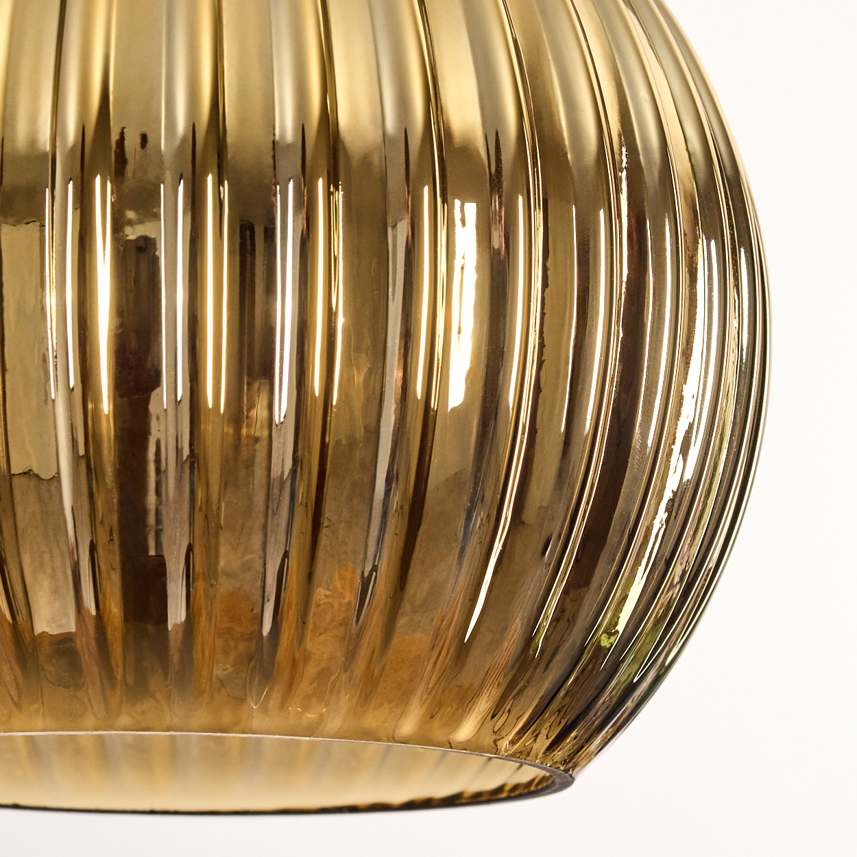 Nahaufnahme eines goldenen, gerippten Glasobjekts vor weißem Hintergrund. Das Glas reflektiert Licht und erzeugt Glanzlichter und Schatten.