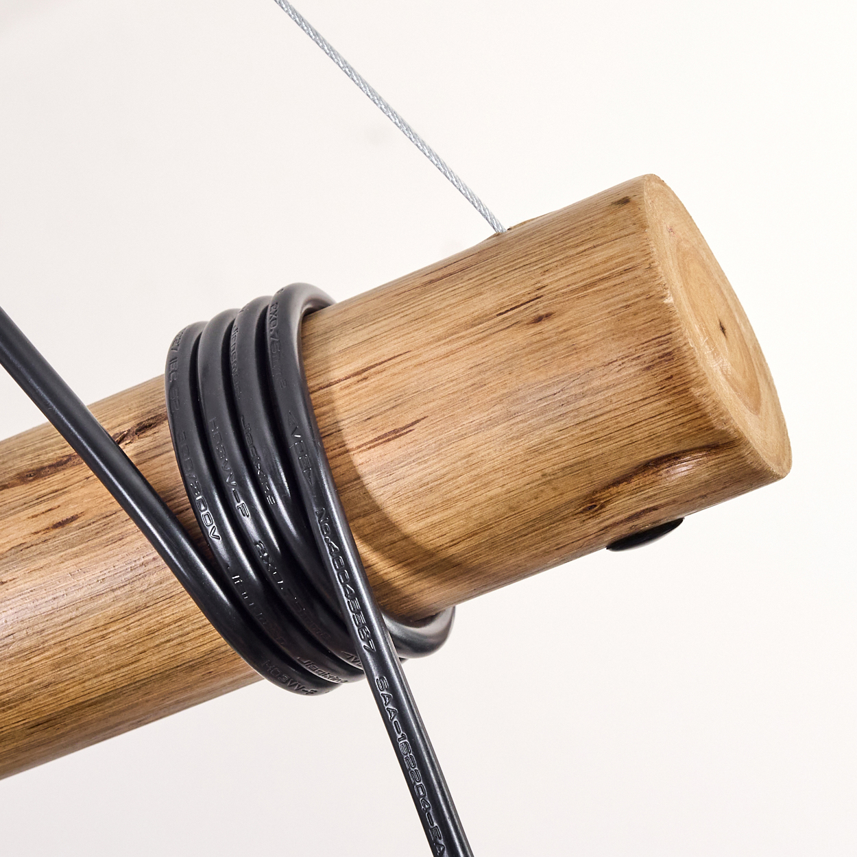Ein Holzstamm mit schwarzen Kabeln umwickelt. Ein dünner Metalldraht ist am Holz befestigt. Weißer Hintergrund.