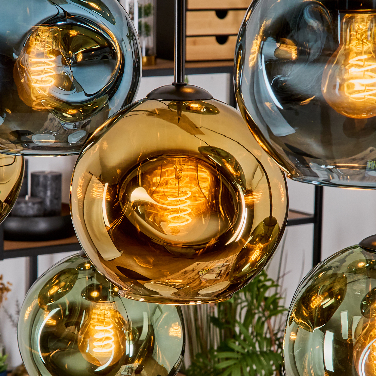 Nahaufnahme von kugelförmigen Glas-Pendelleuchten. Jede Kugel hat eine warme Glühbirne. Die Kugeln sind in Gold- und Blautönen gehalten.