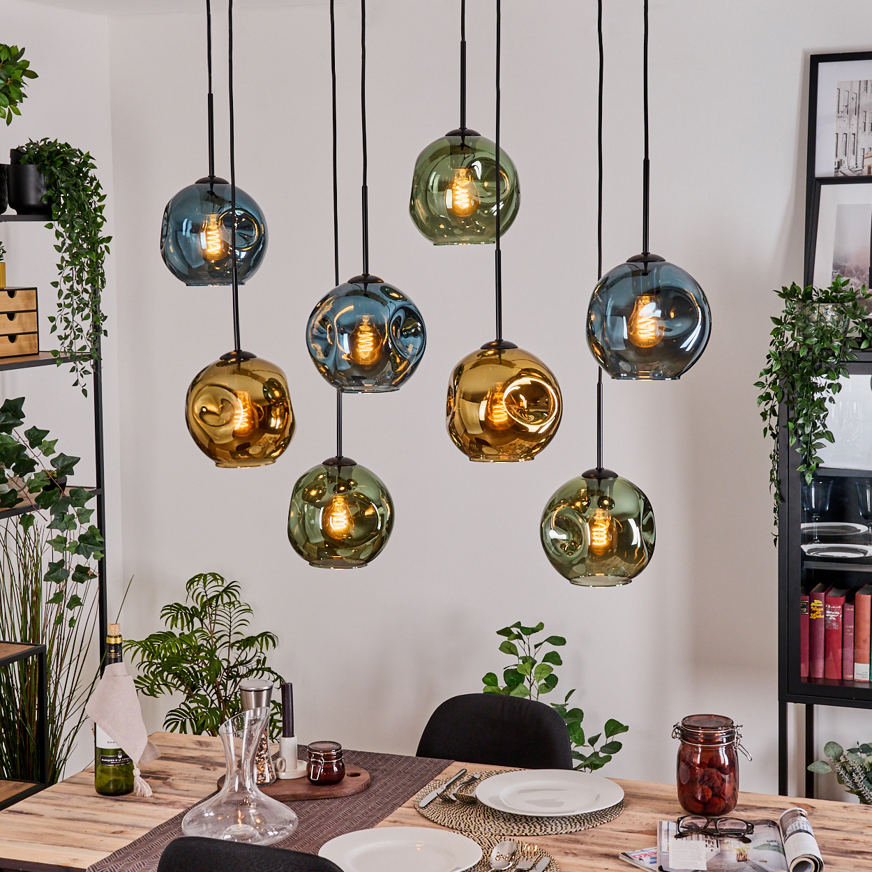 Esszimmer mit mehreren hängenden Glaskugelleuchten. Tisch für eine Mahlzeit gedeckt. Regale mit Pflanzen und Dekoration sind sichtbar.