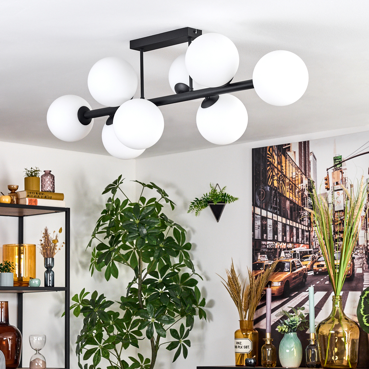 Eine moderne schwarze Deckenleuchte mit weißen Kugelleuchten. Eine große Pflanze, Regale mit Dekor und ein Stadtbild sind sichtbar.