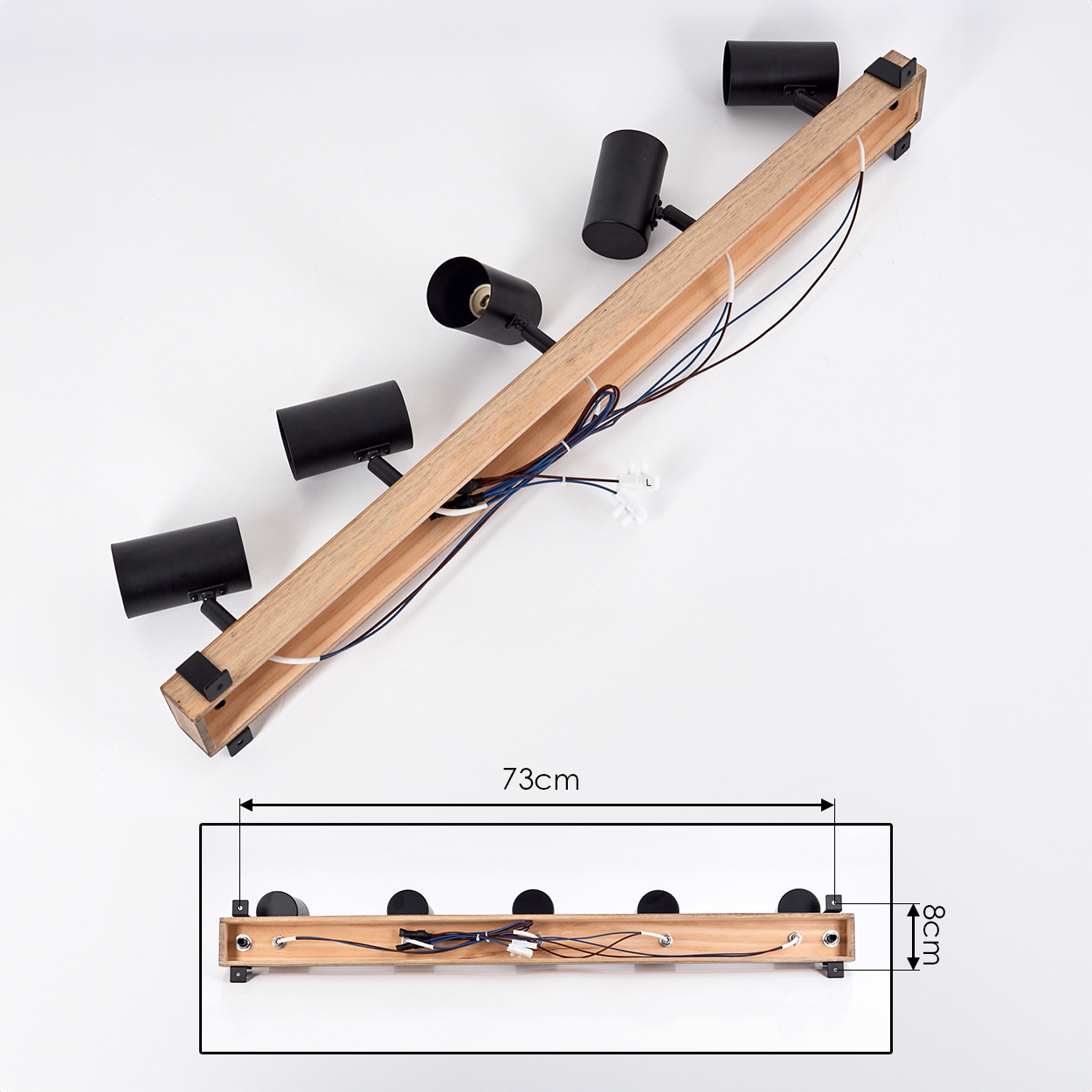 Eine hölzerne Schienenleuchte mit vier schwarzen Strahlern. Drähte und Abmessungen sind ebenfalls sichtbar. Sie ist 73 cm lang und 8 cm breit. Weißer Hintergrund.