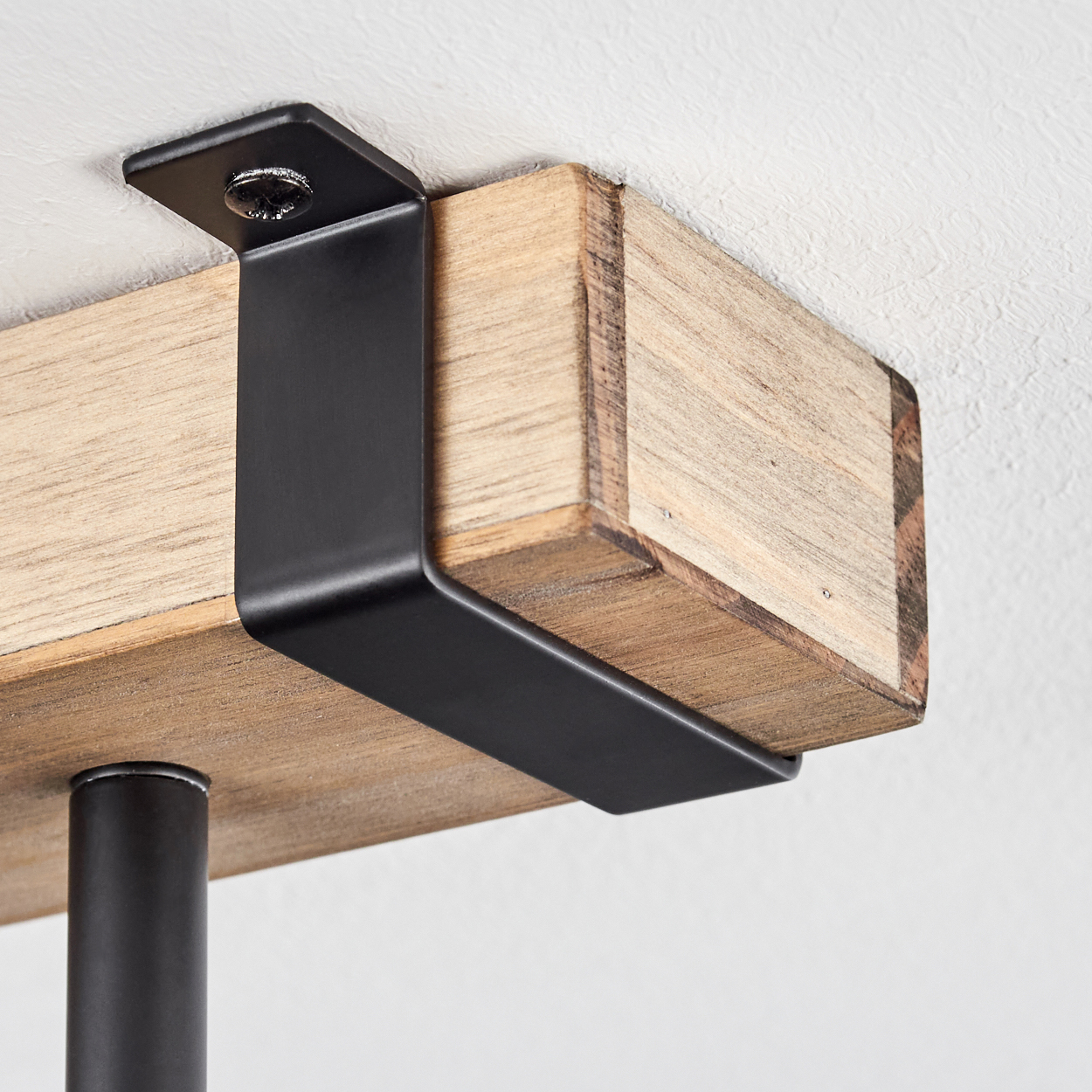 Nahaufnahme eines Holzbalkens, der von einer schwarzen Metallhalterung gehalten und an einer weißen Decke befestigt ist.